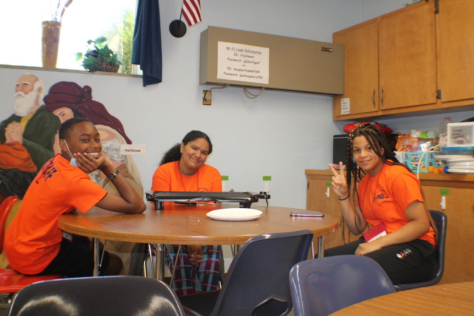 Three people in orange shirts sitting around a table in a room, smiling and chatting