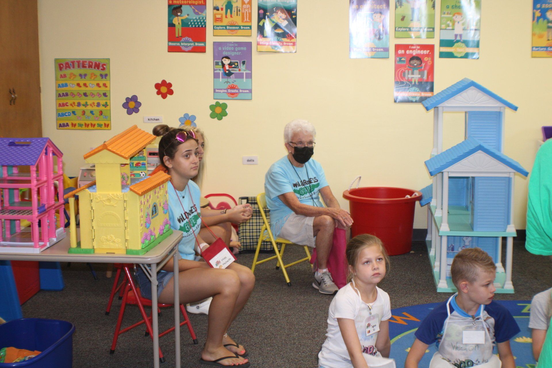Classroom with children and adults seated among colorful play structures and posters