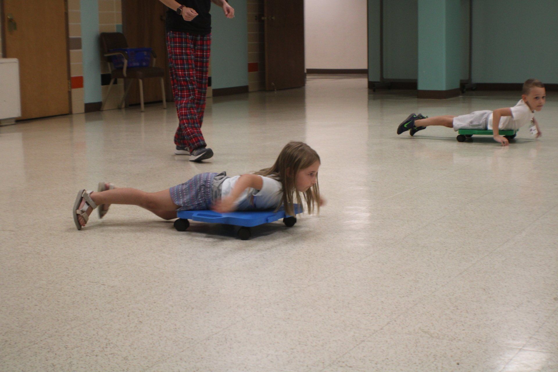 Children doing floor exercises in a gymnasium, one on a blue mat and another nearby.
