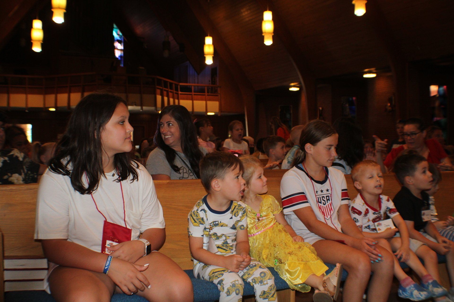 Children seated in a dimly lit auditorium, watching something off-camera