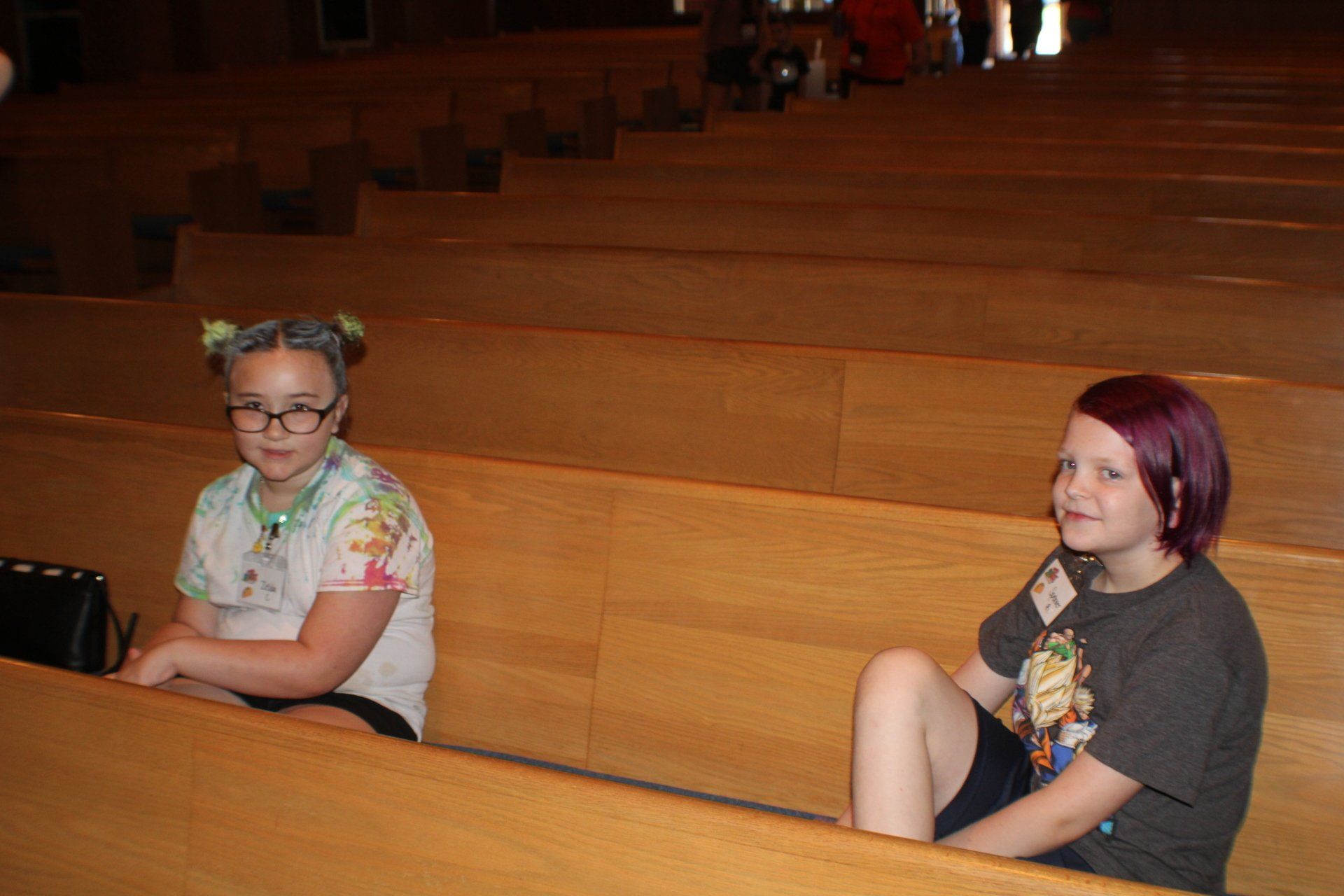 Two people sitting apart on wooden church pews, looking toward the front.