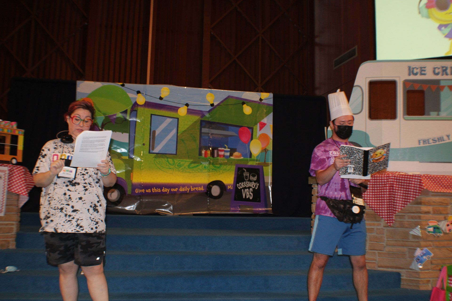 People on a stage holding papers, with colorful display boards and a model ice cream truck behind them.