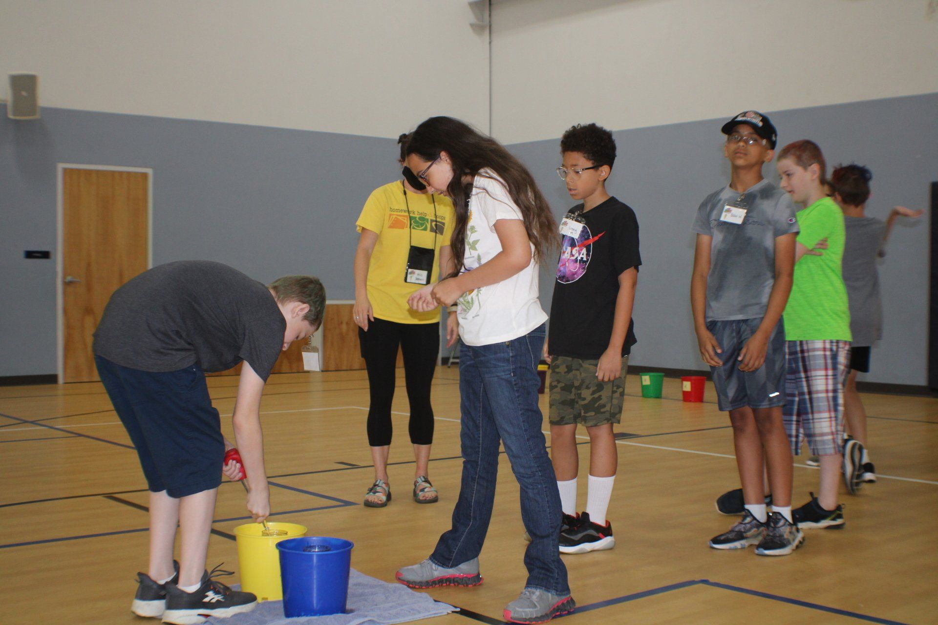 People gathered in a gym, watching one person bend over a bucket during an activity.