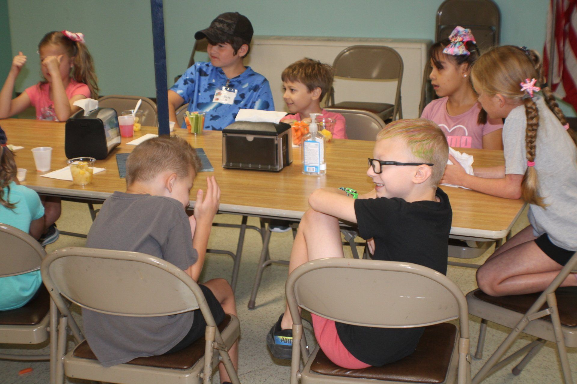 Children seated around a table, drawing and crafting with supplies in a classroom or activity room.