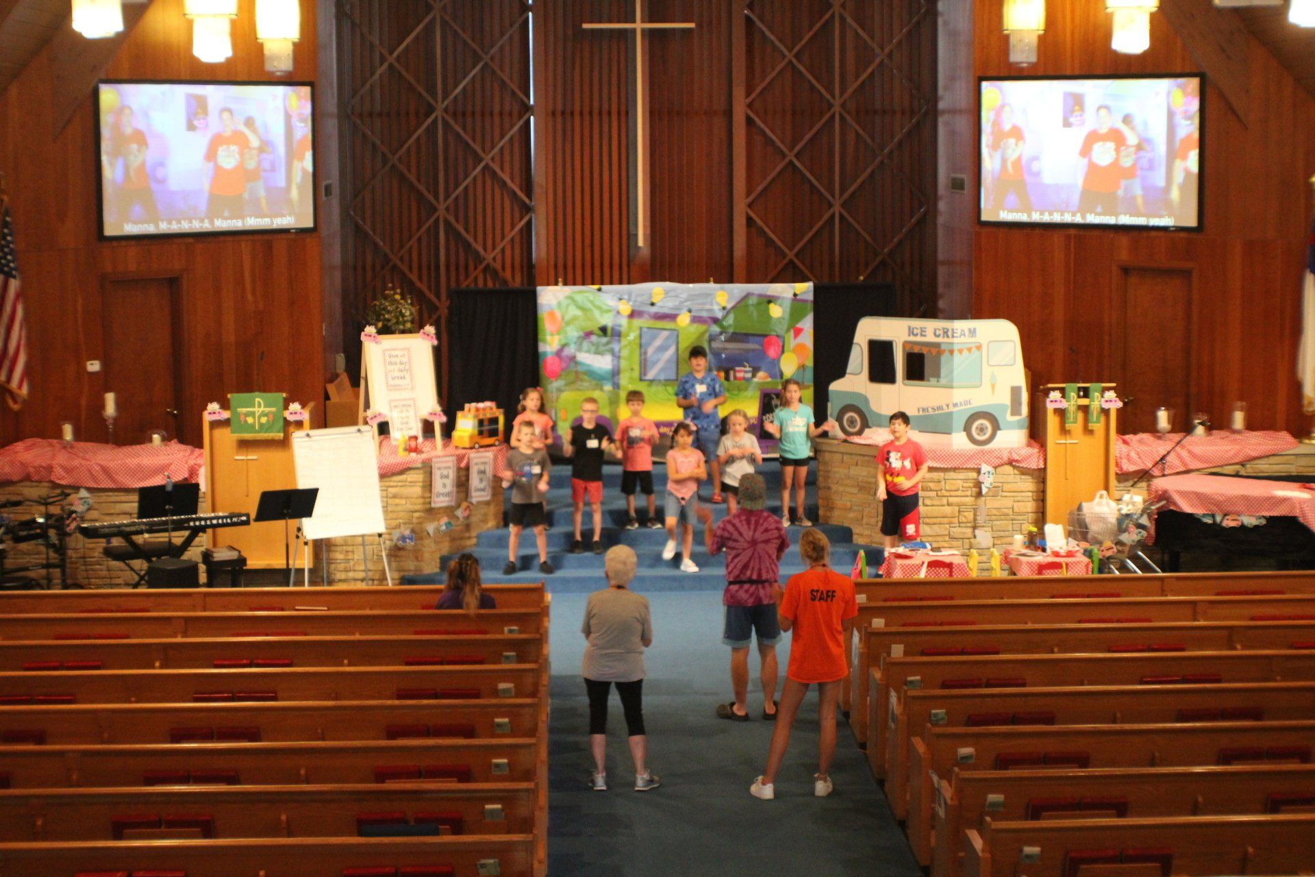 People standing on a church stage with children’s decorations and a small white vehicle backdrop
