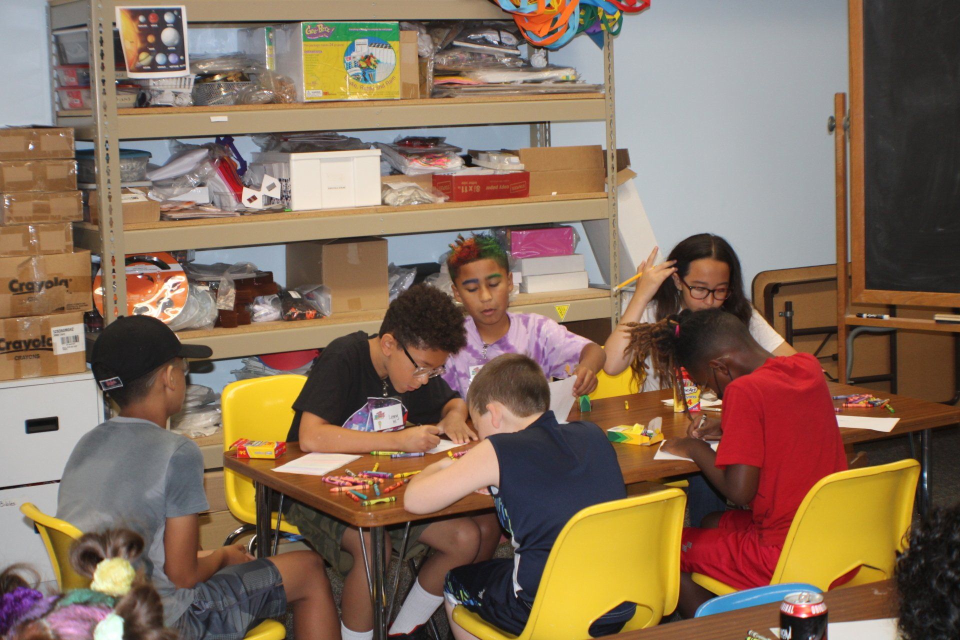 Children seated around a table crafting in a colorful classroom with shelves of supplies