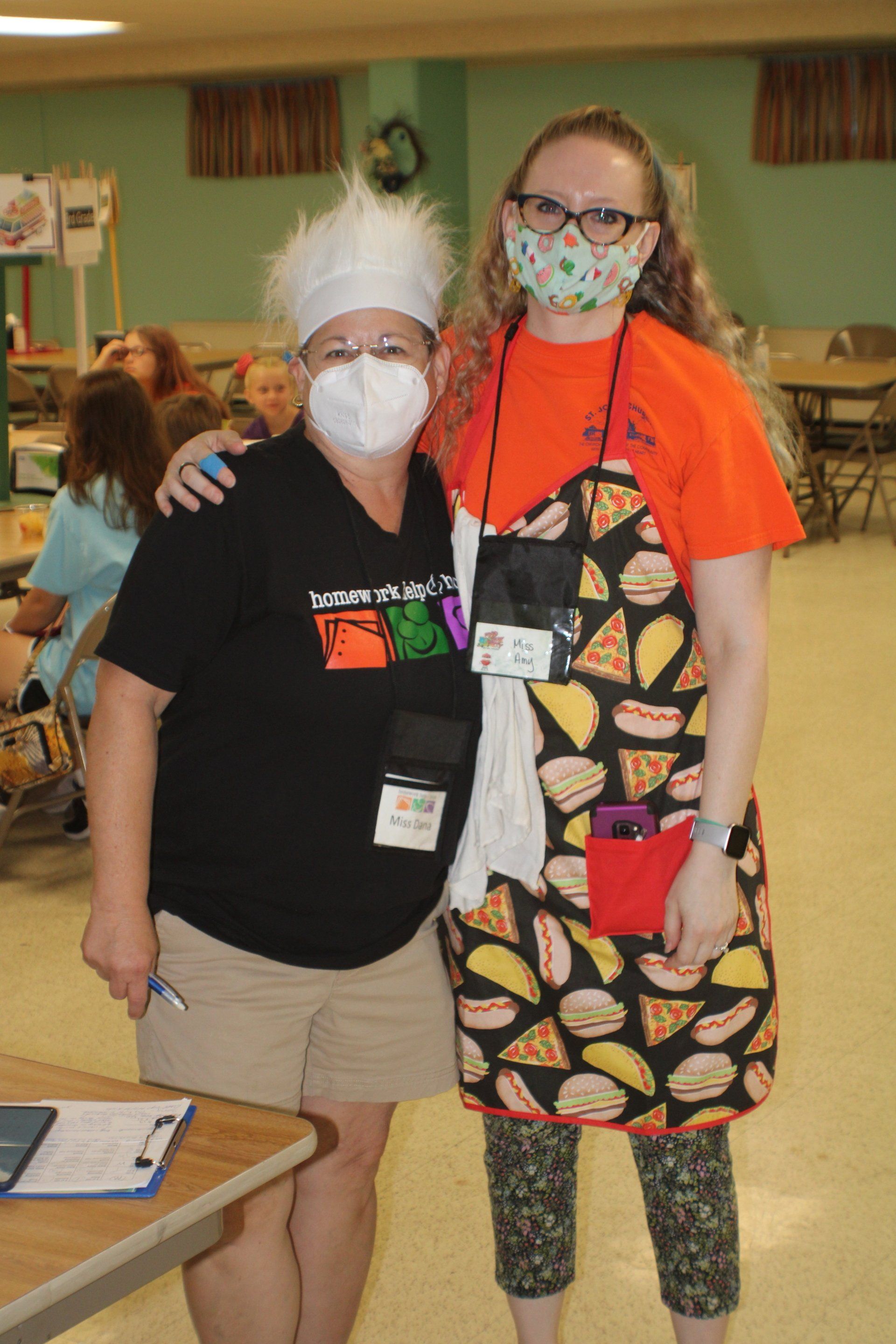 Two masked people pose indoors in a classroom