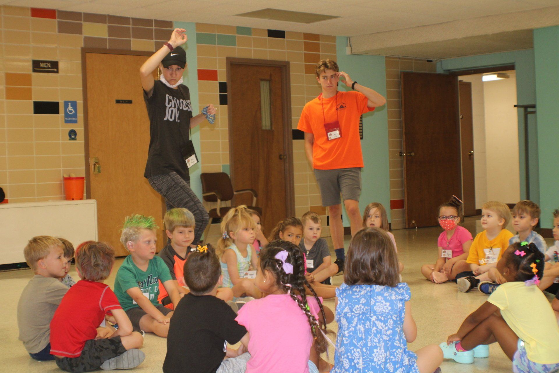 Two presenters speaking to seated children in a school hallway
