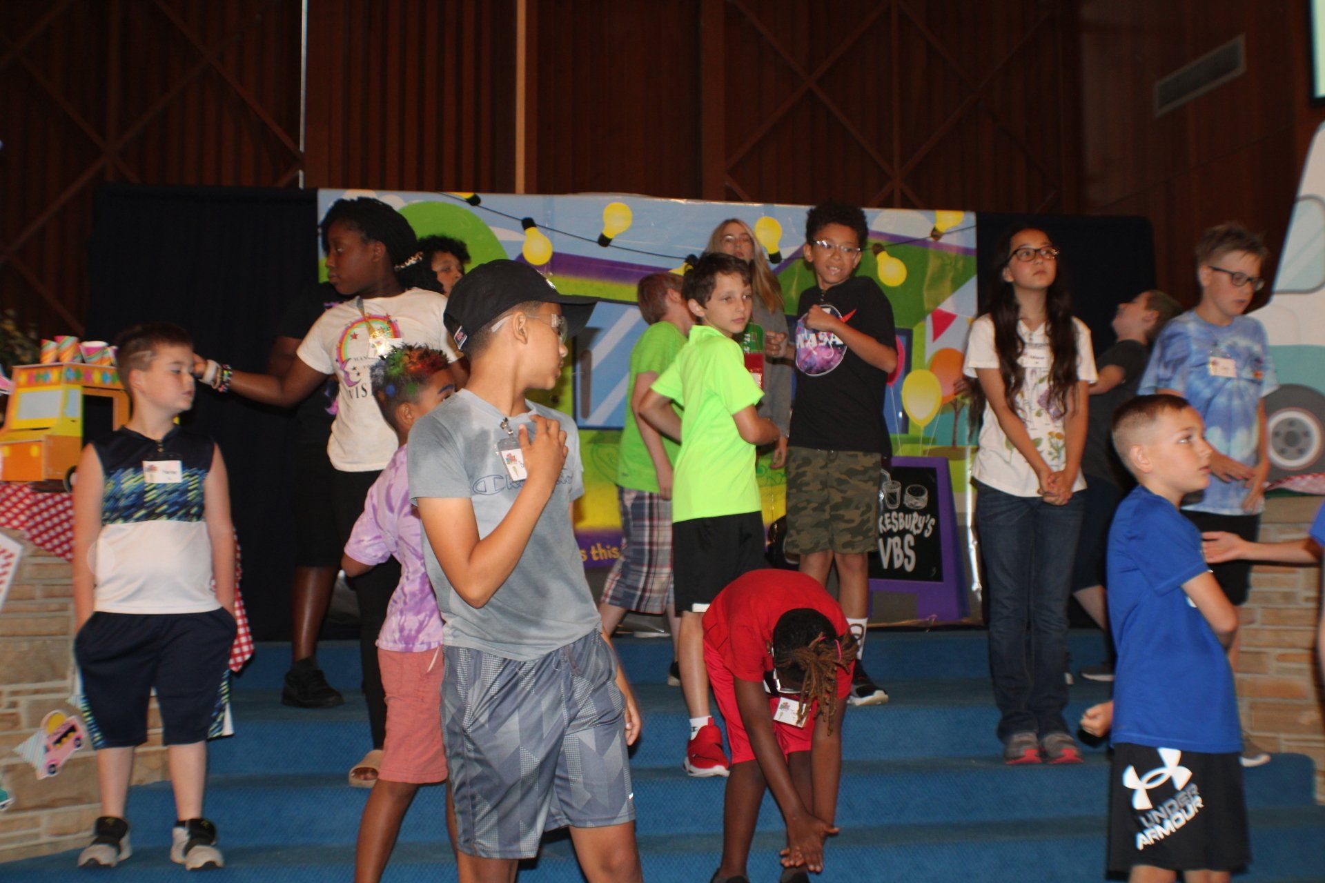 Children performing on a stage, with colorful props and a dark backdrop.