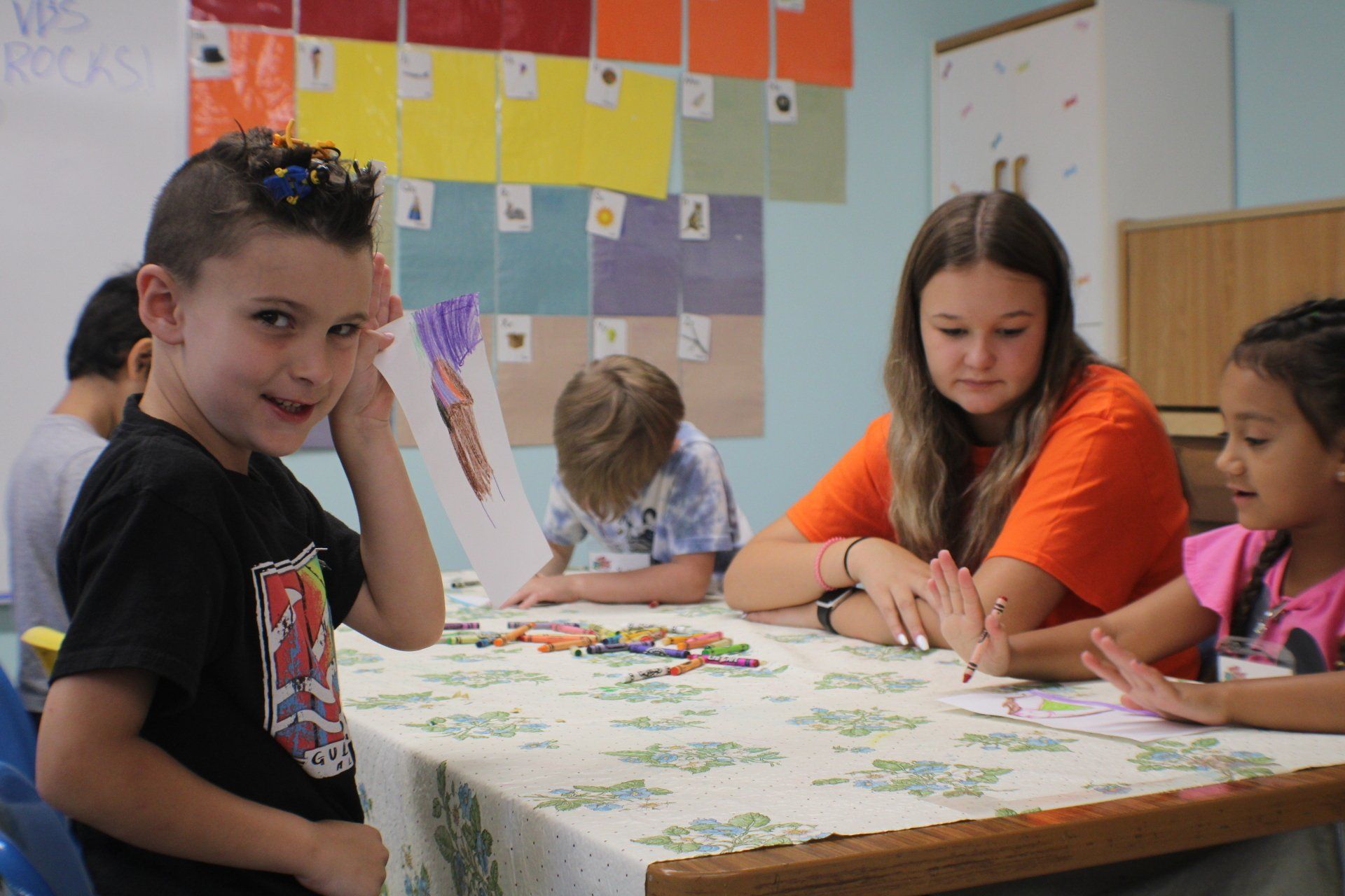 Children working on a puzzle at a classroom table with a teacher nearby