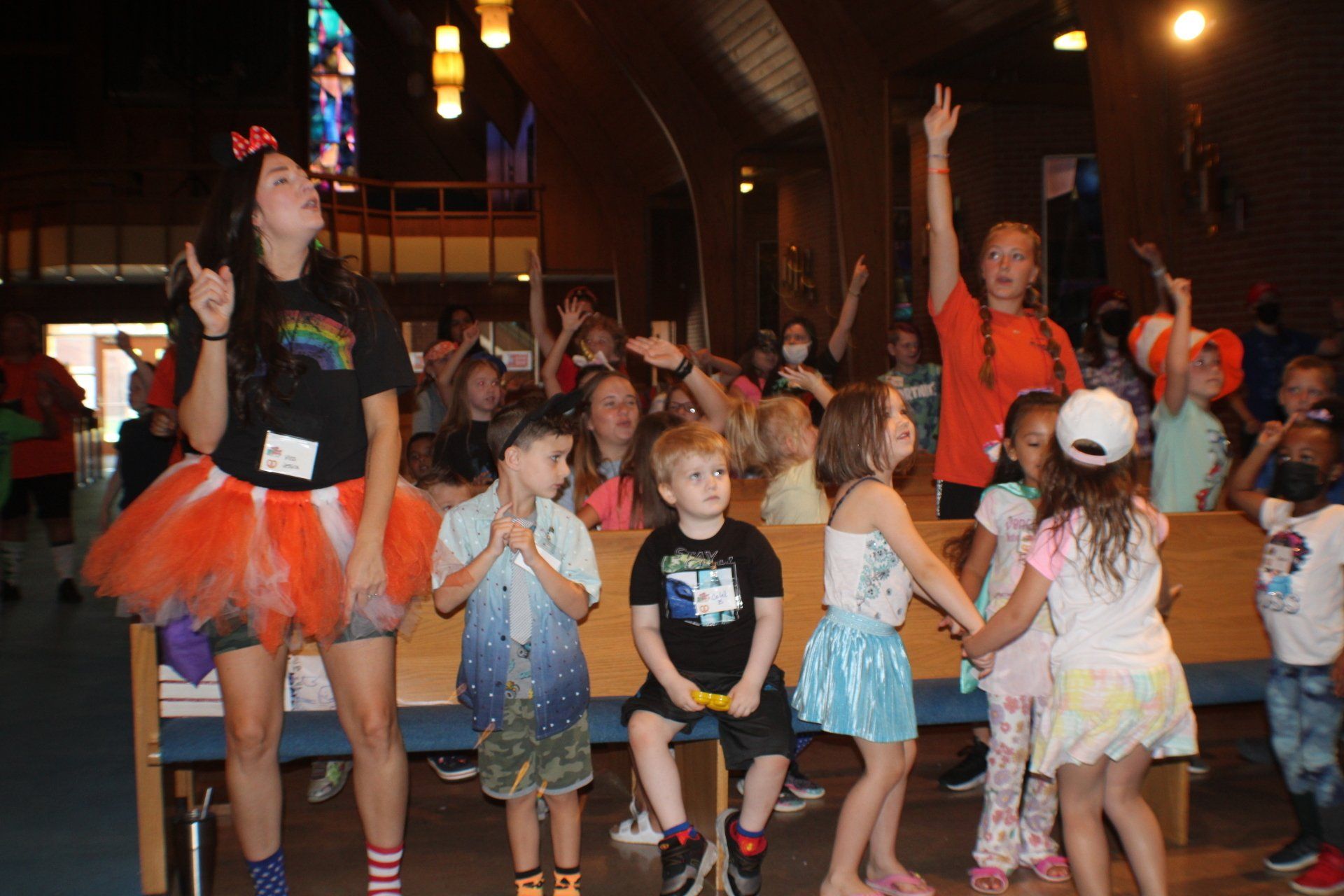 Children dancing outdoors at night, with one adult leading a playful group in orange tutus.