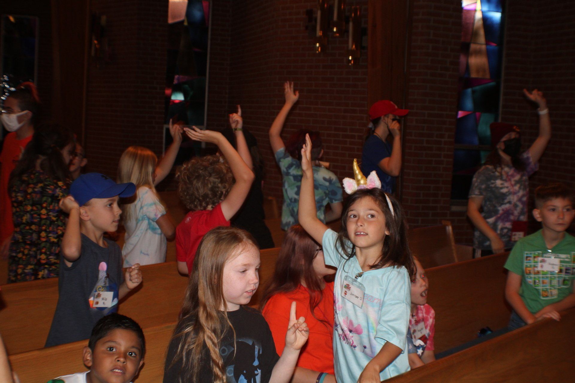Children sitting in church pews, raising their hands during a group activity