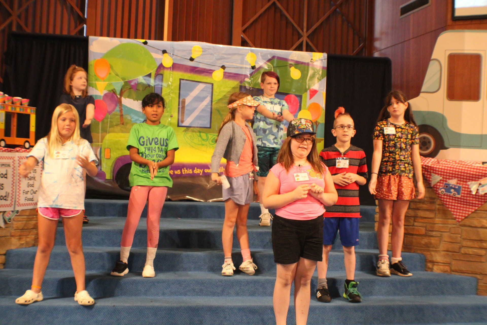 Children on a stage, posing in colorful clothes with a bright painted backdrop.