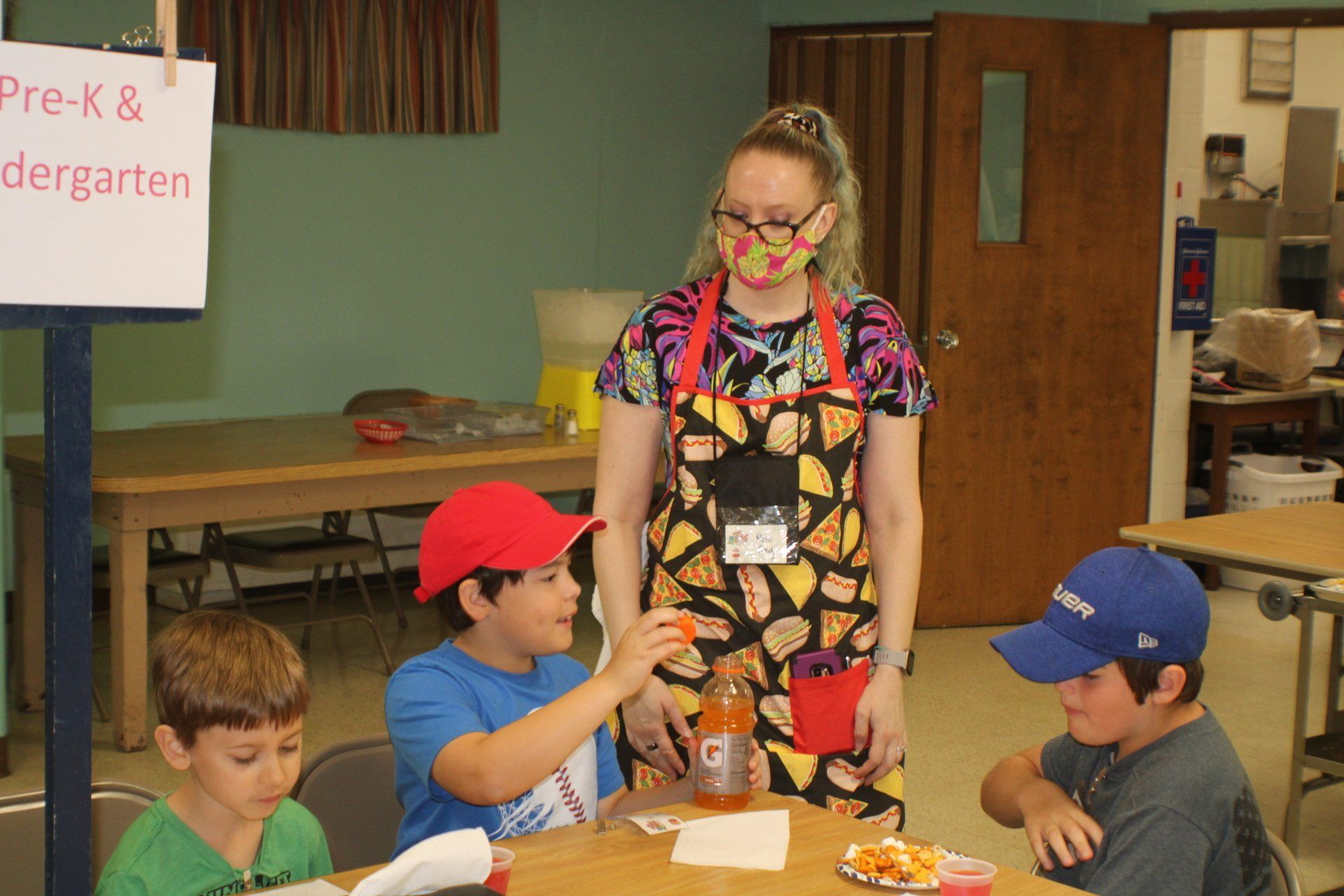Teacher with students at a table in a classroom, with a sign reading “Pre-K & Kindergarten.”