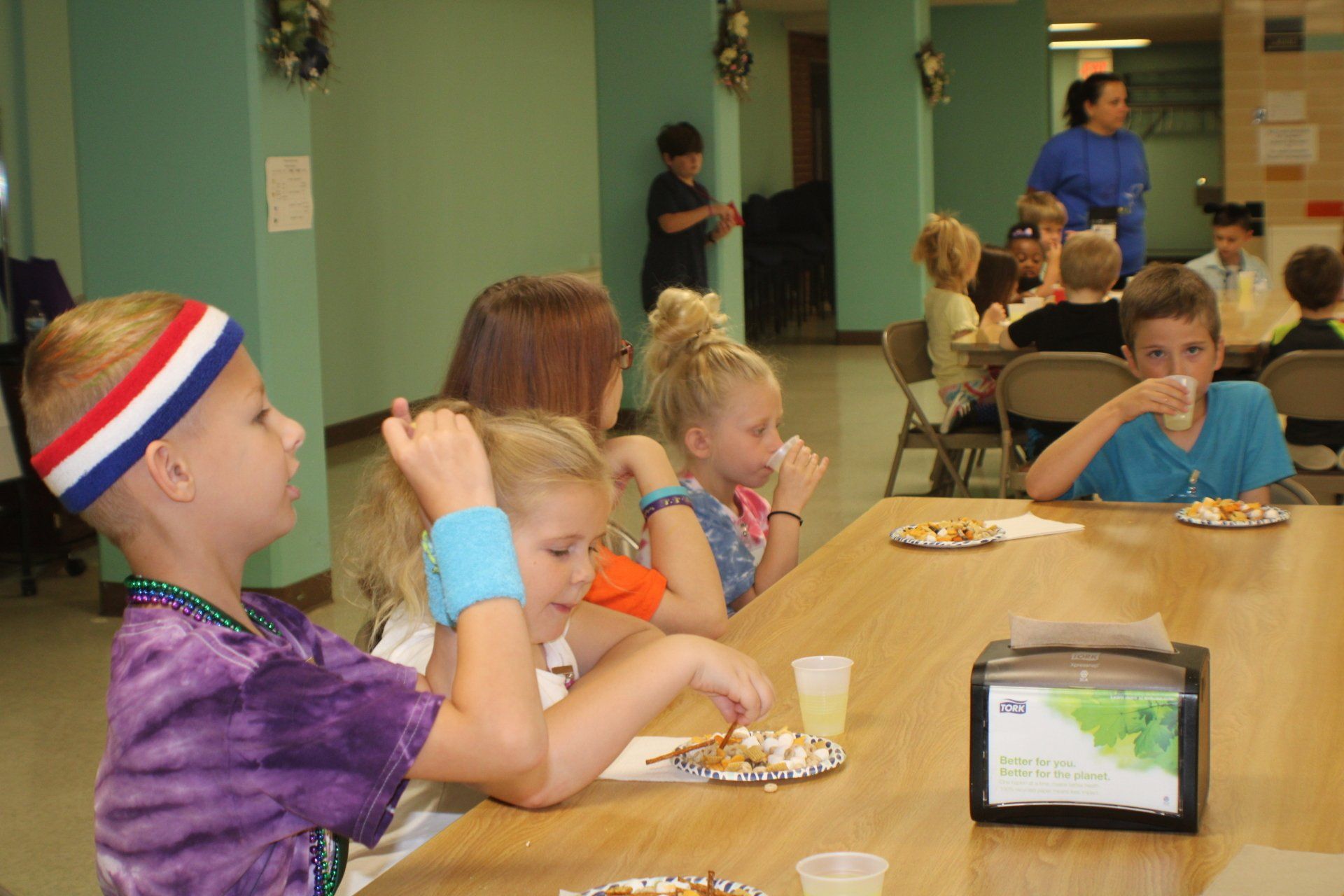 Children eating at a cafeteria table, with a tablet propped up in the foreground.