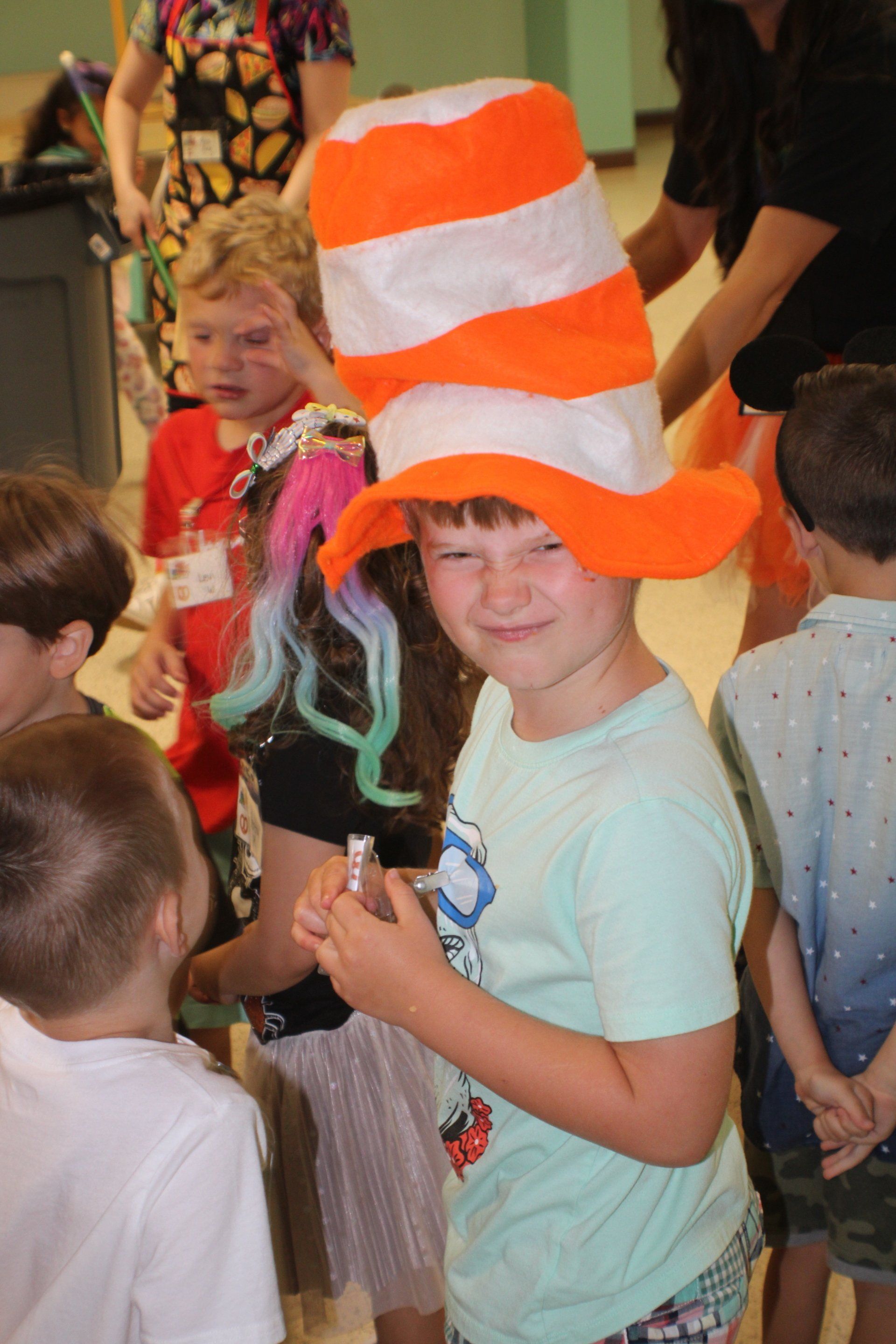 Child wearing a tall orange-and-white striped hat at a crowded indoor event