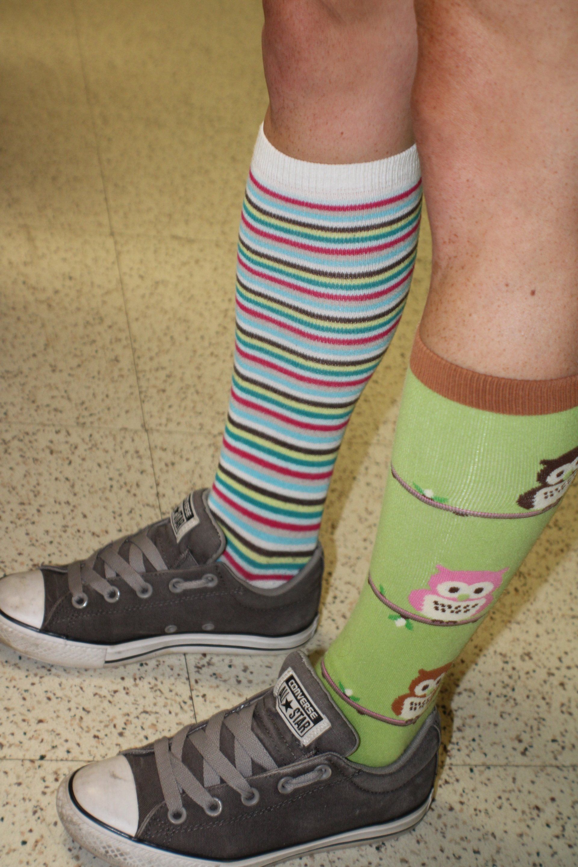 Person wearing mismatched knee-high socks and black sneakers on a tiled floor.
