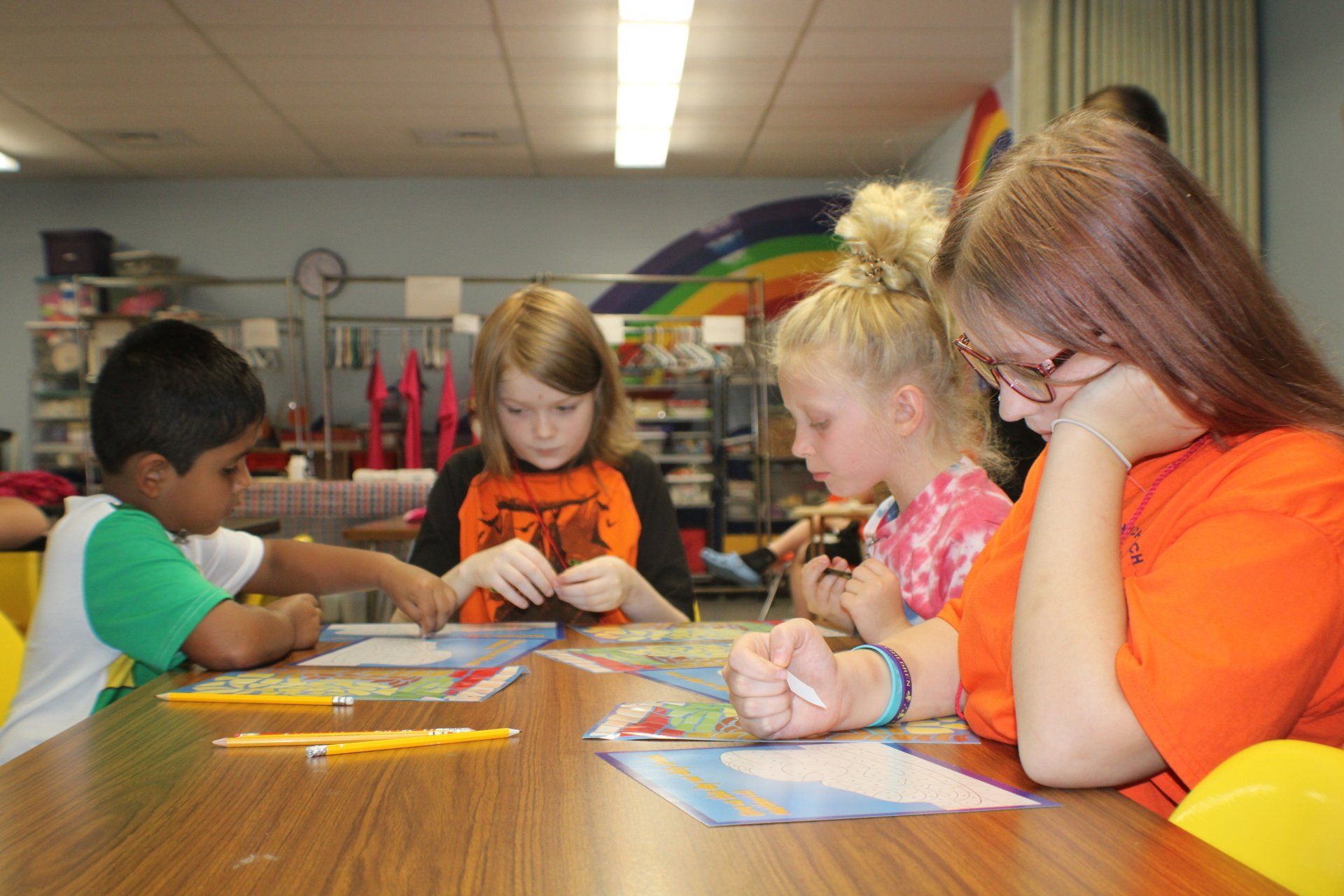 Children doing an art activity at a table in a classroom, drawing with crayons and markers.
