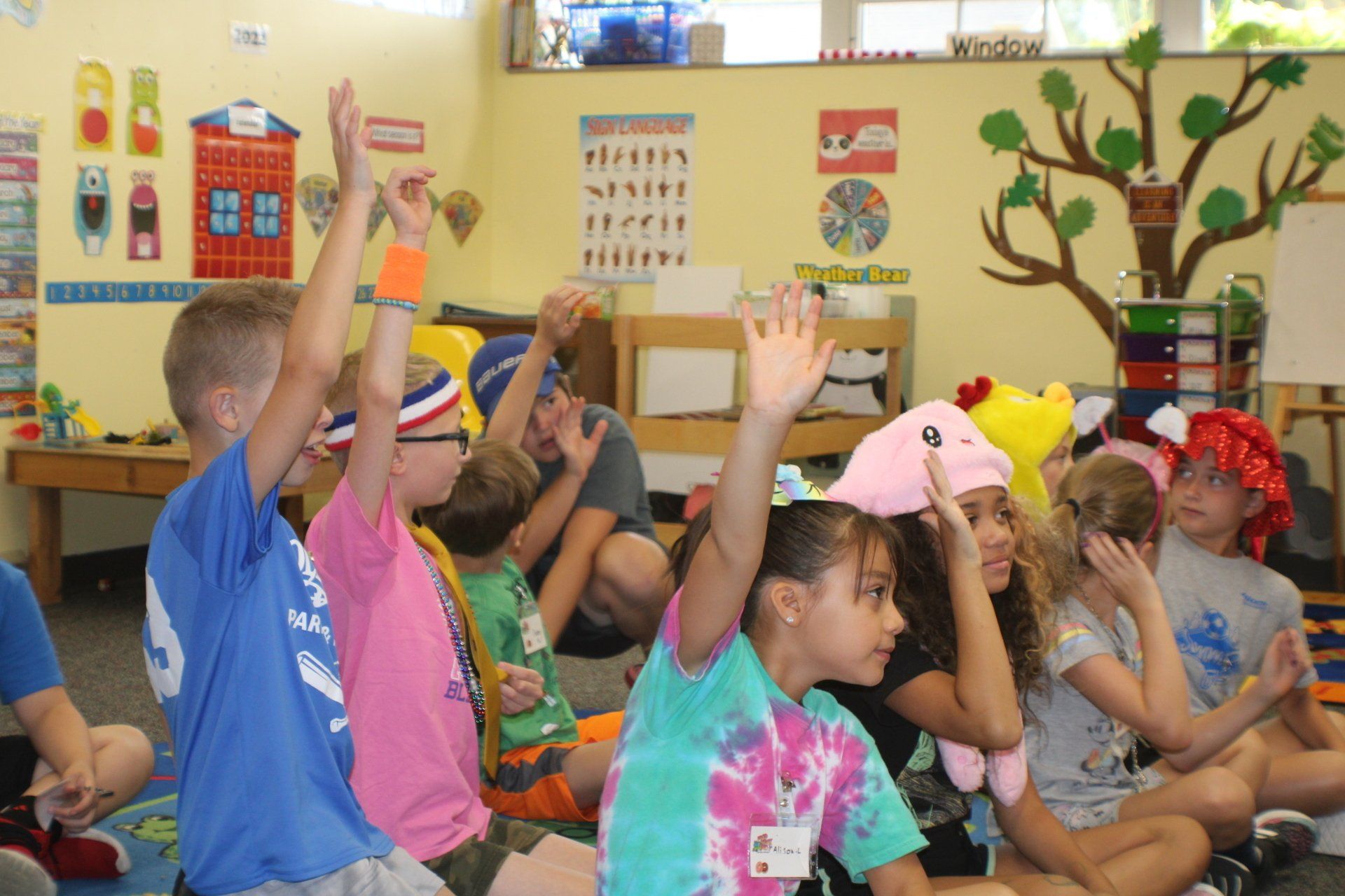 Children sitting cross-legged in a classroom, raising their hands during a lesson