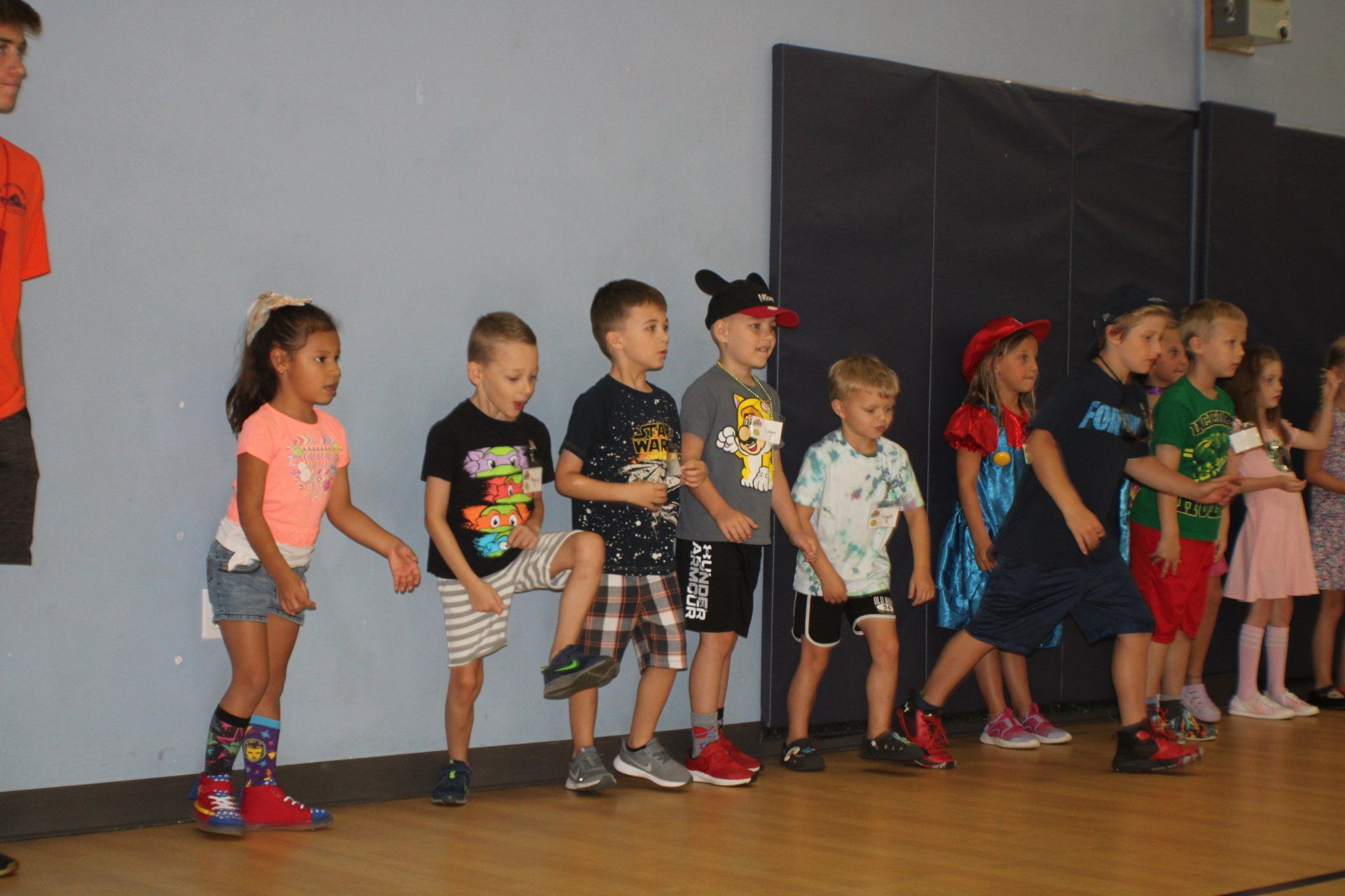 Children standing in a line on a stage, dressed in colorful outfits during a performance