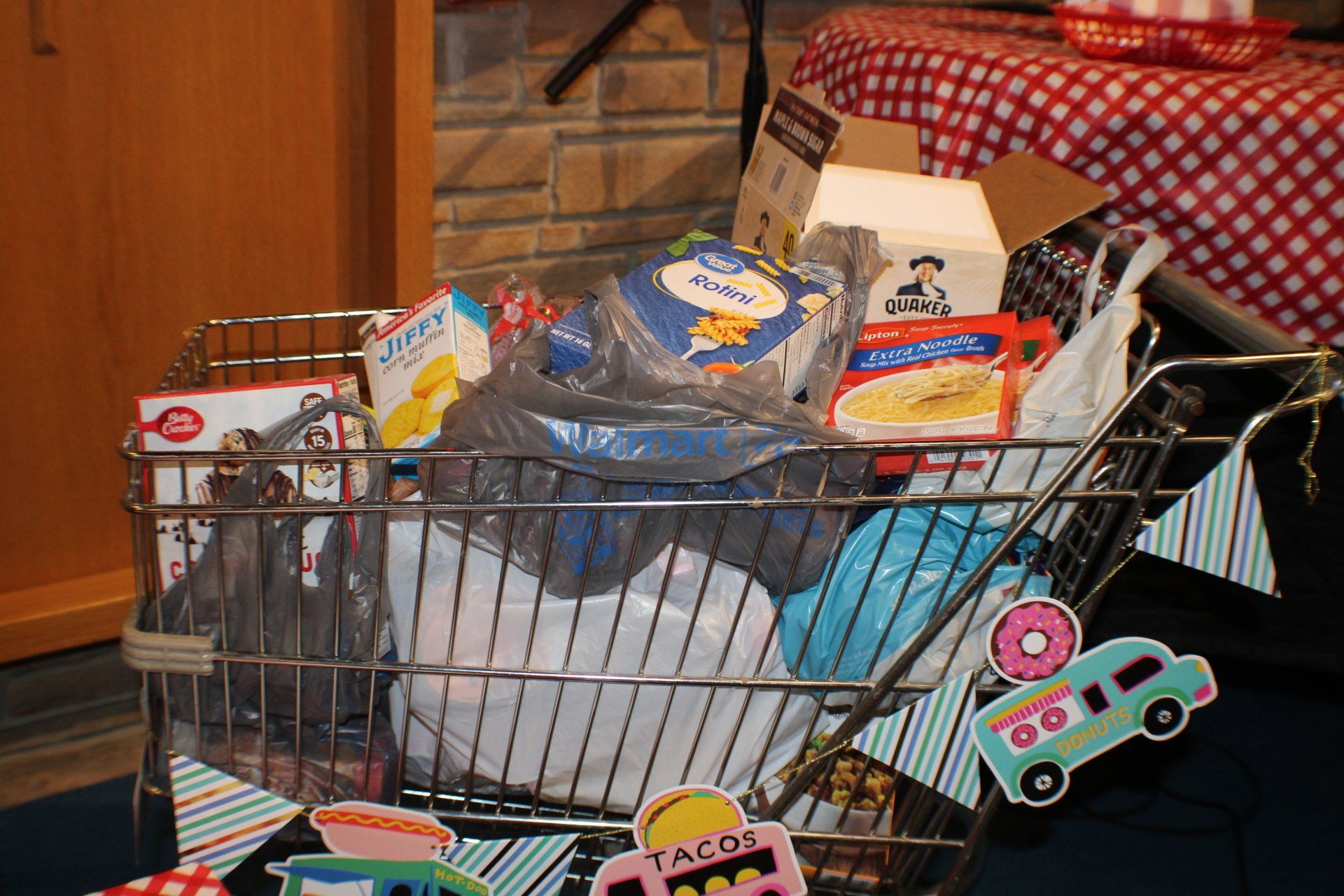 A wire shopping cart piled with groceries, toys, and household items in a home interior.