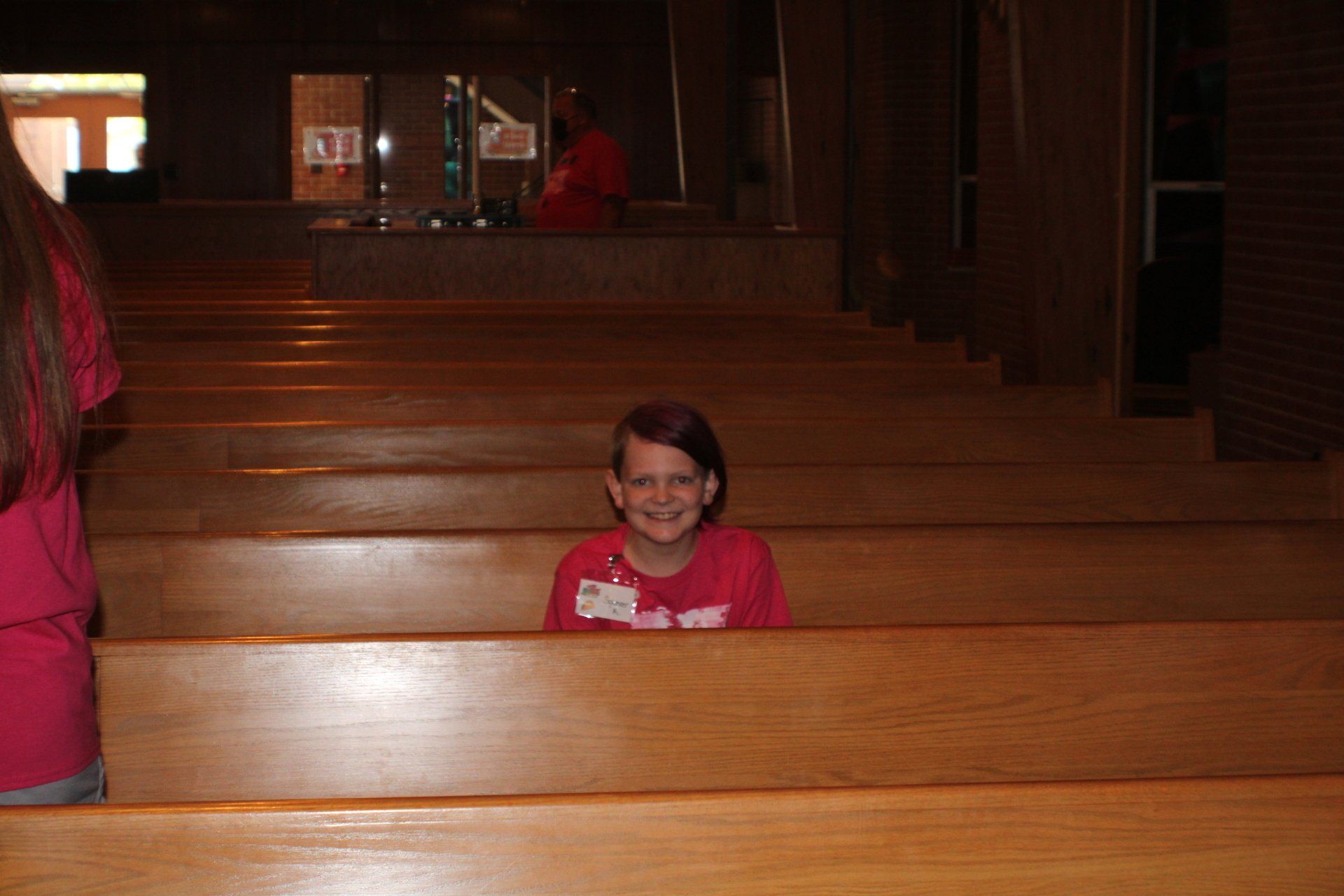 Person in a red shirt sitting in a wooden church pew, centered in a dimly lit sanctuary.