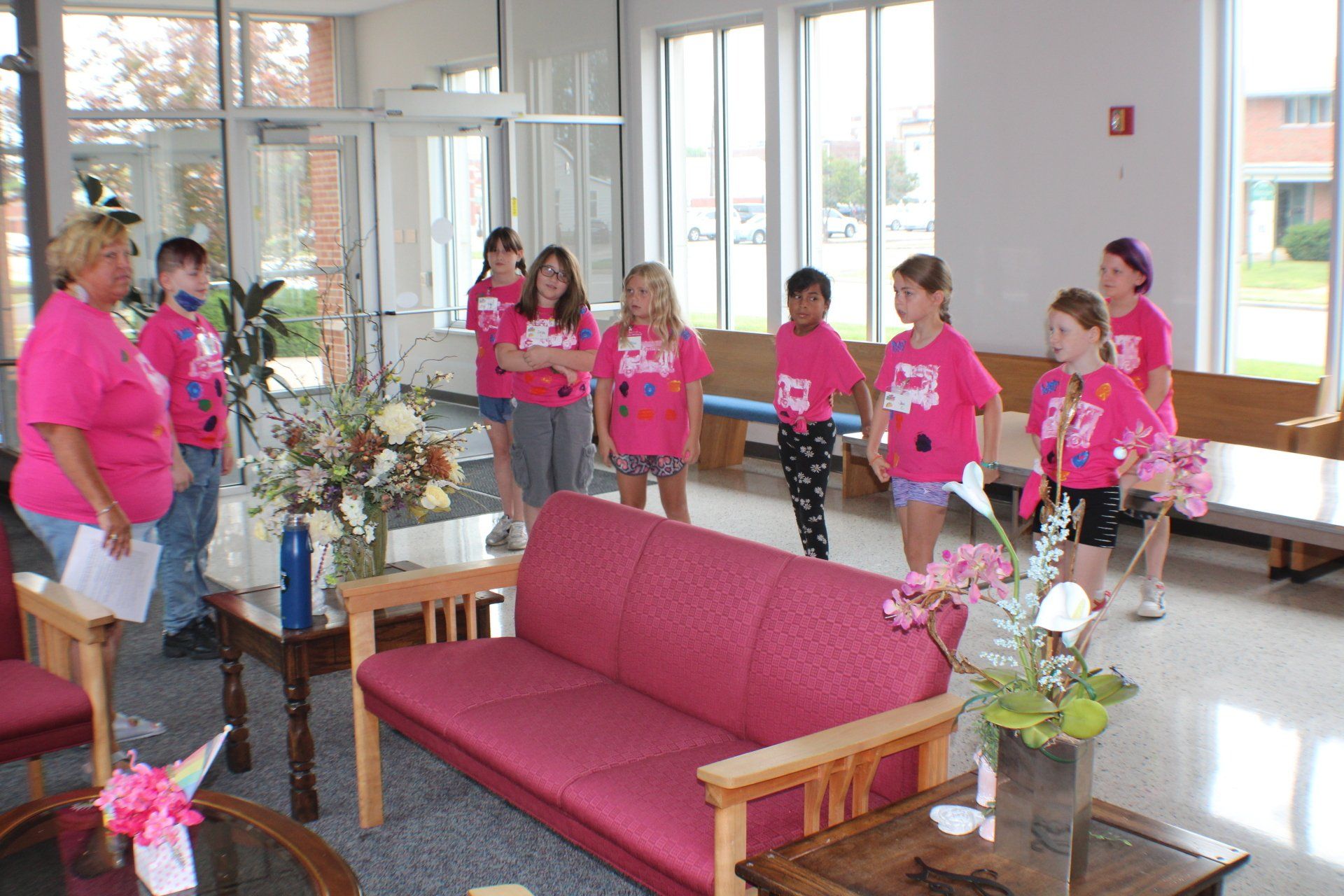 Group of people in bright pink shirts standing in a lobby with sofas and tables with flowers
