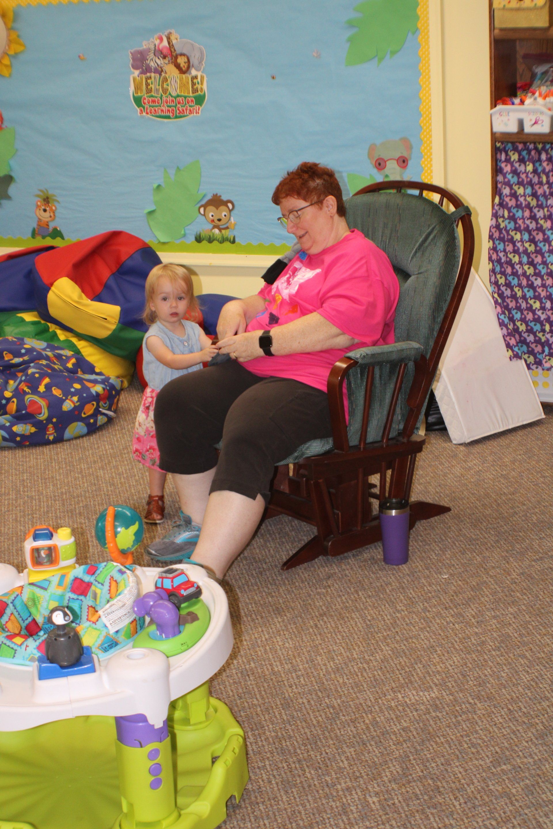 Woman and child seated in a playroom, with toys scattered around them.
