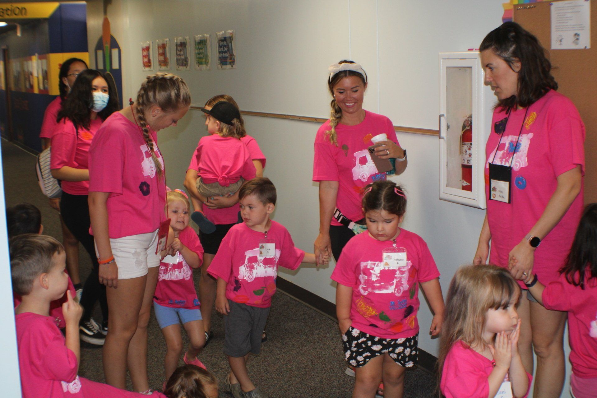 Children in pink shirts standing in a hallway, some holding cups and a snack bag