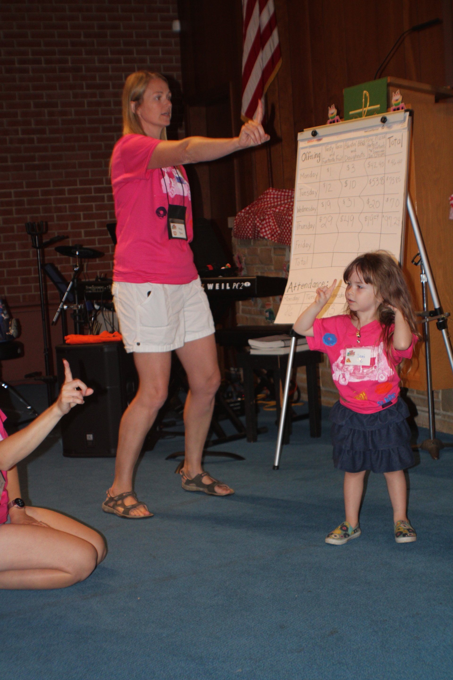 Woman and child dancing in a church hall, with a whiteboard and flag in the background