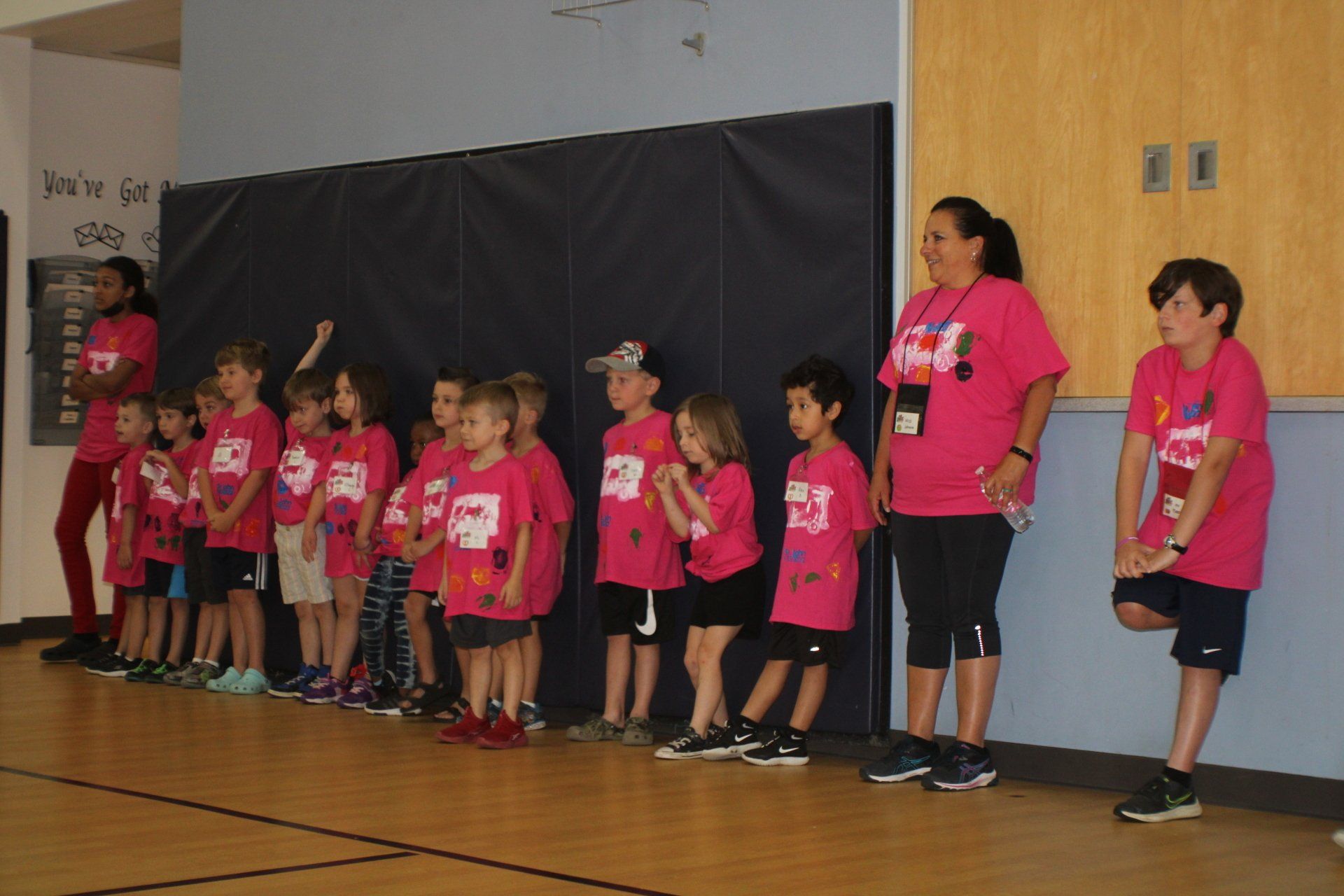 Children in pink shirts standing on a gym stage during an event