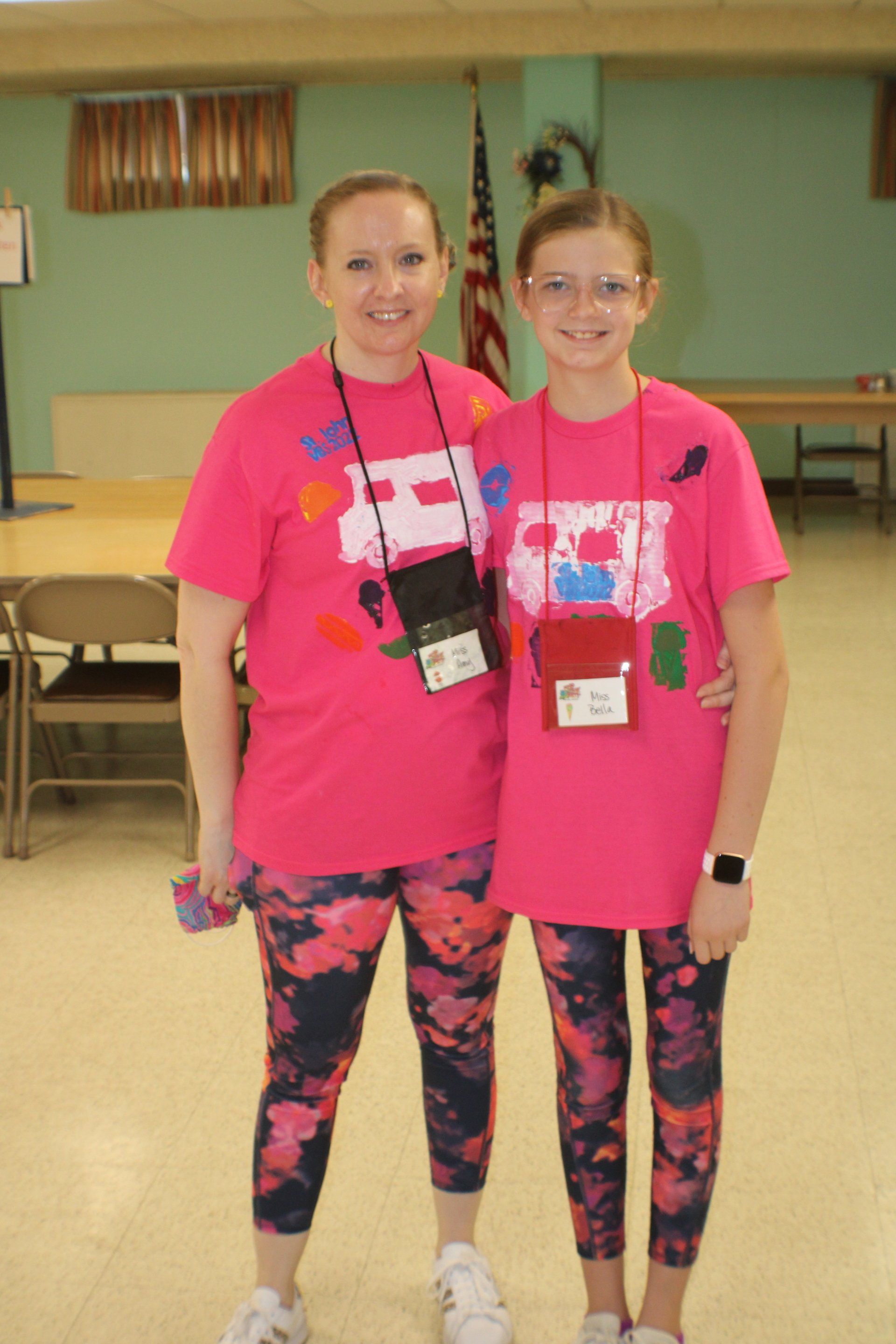 Two people in bright pink shirts and patterned leggings standing in a gym or hall