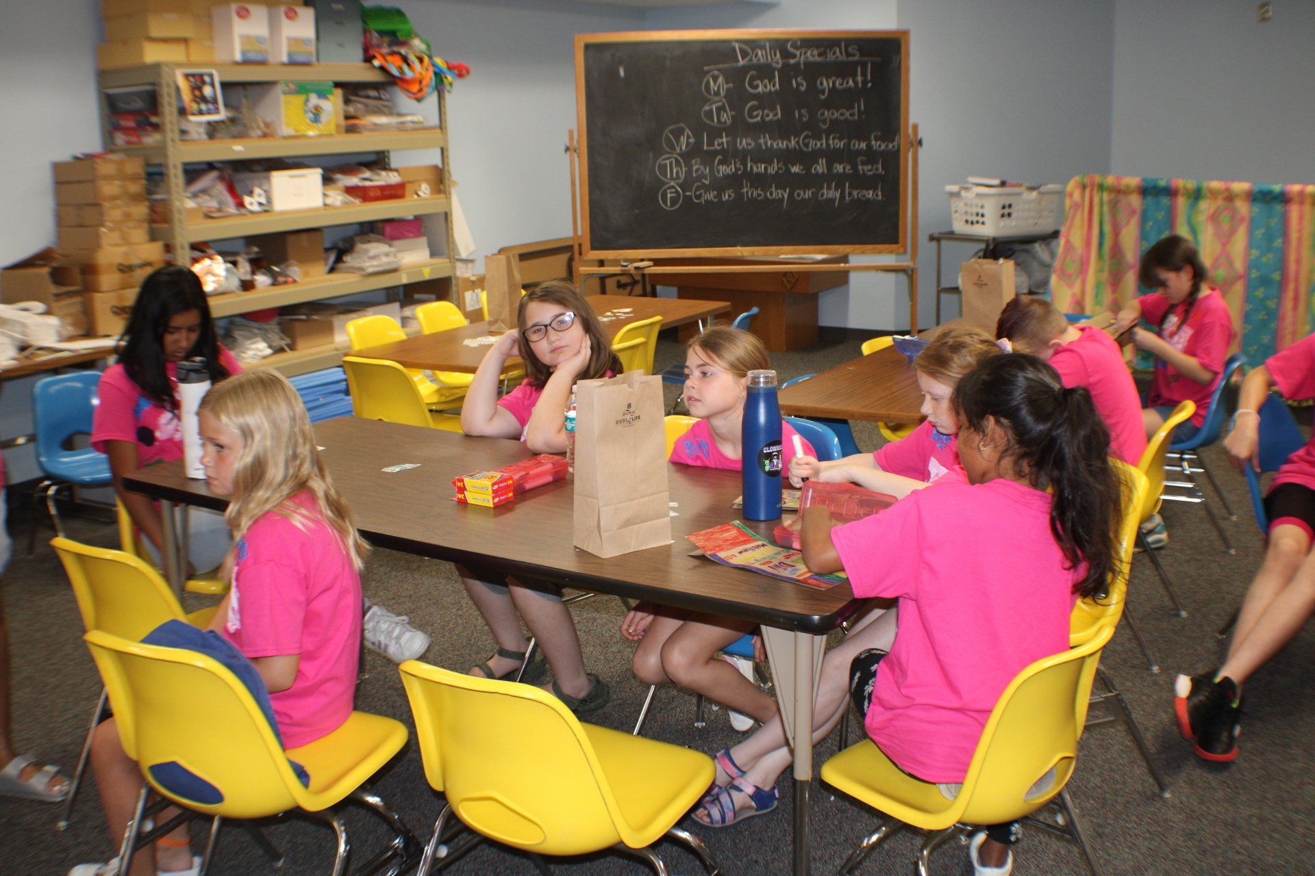 Children seated at a table in a classroom, working with books and papers during a group activity