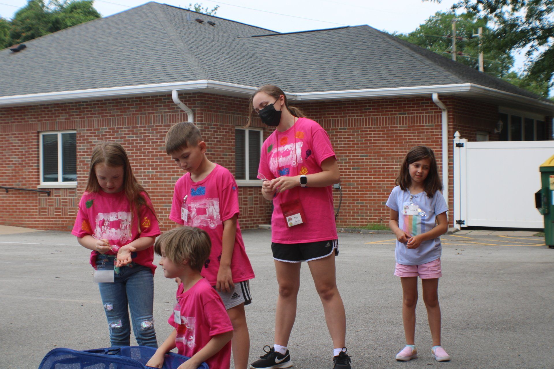 Five children in pink shirts standing outdoors in a driveway near a brick house