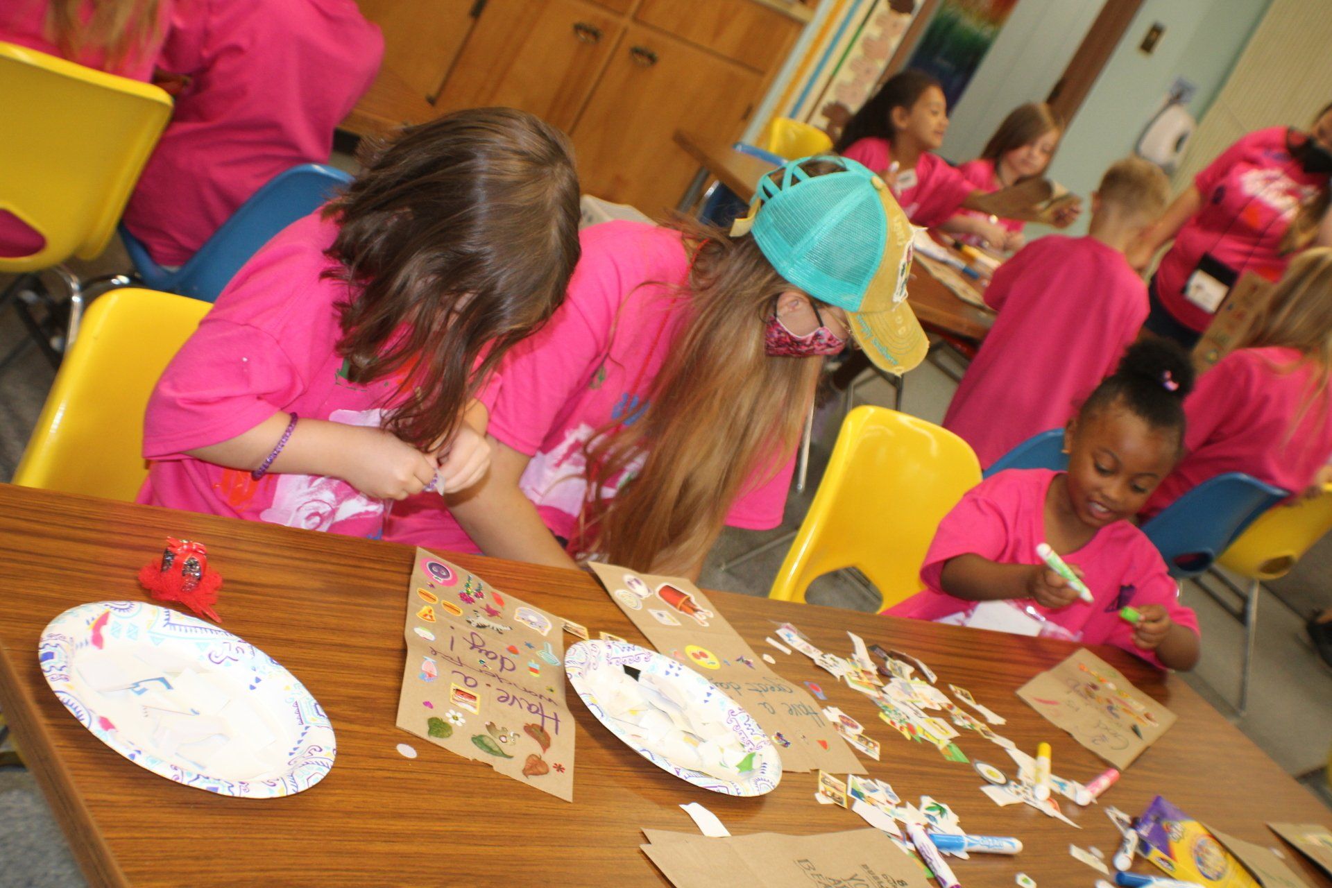 Children in pink shirts doing a craft activity at a table with paper plates and supplies