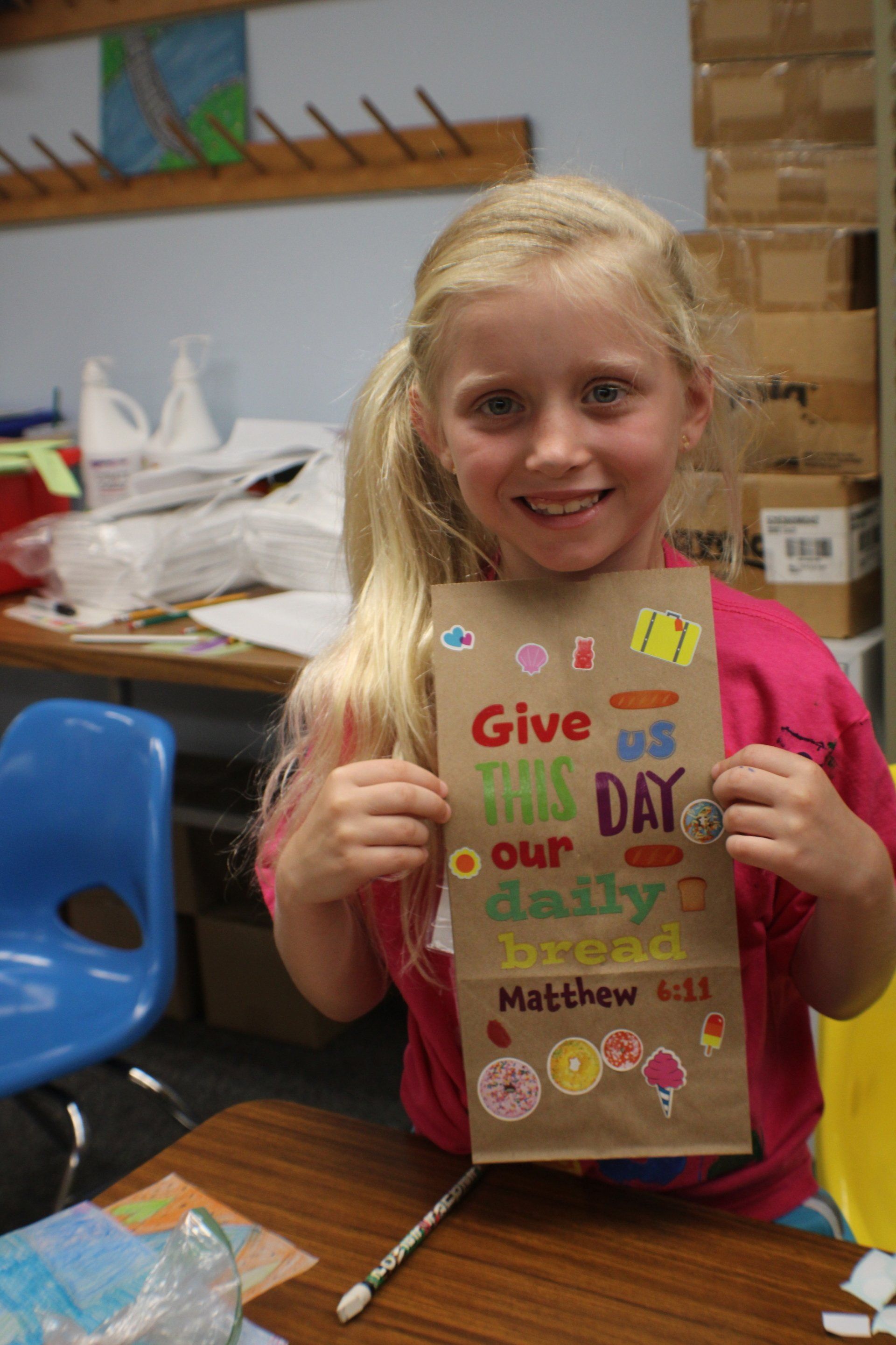 Child holding handmade Father's Day card in a classroom, smiling at the camera.