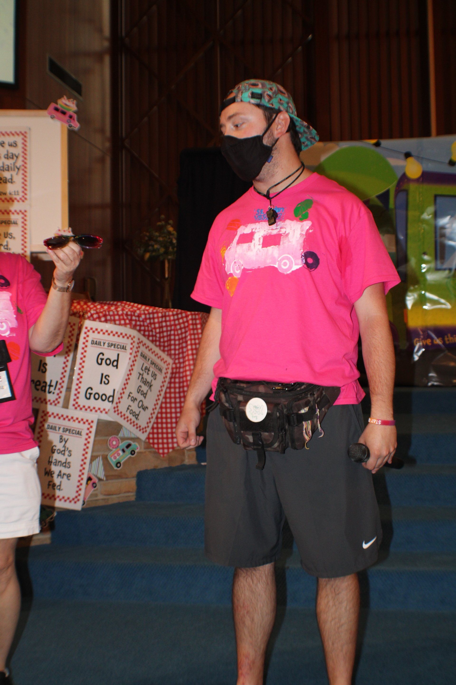 Person in bright pink shirt and black shorts standing indoors at a costume event