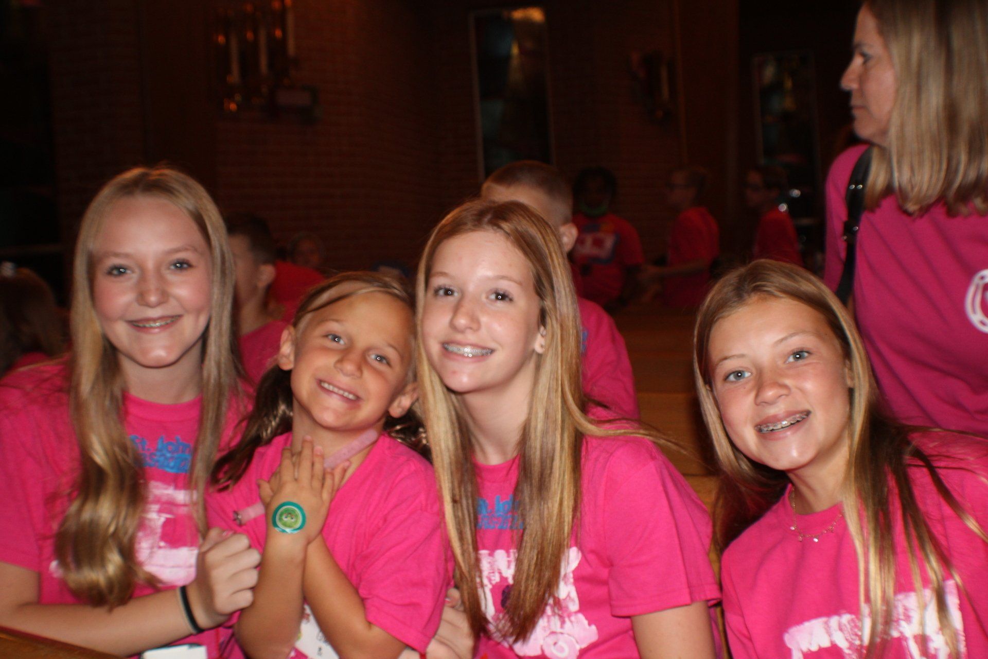 Four smiling kids in bright pink shirts posing indoors at an event