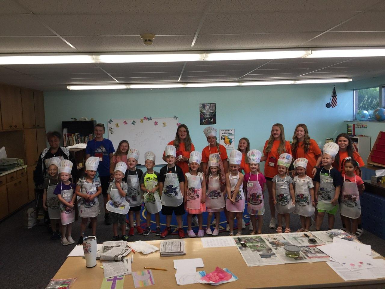 Group of children holding decorated paper bags in a classroom, with crafts laid out on tables.