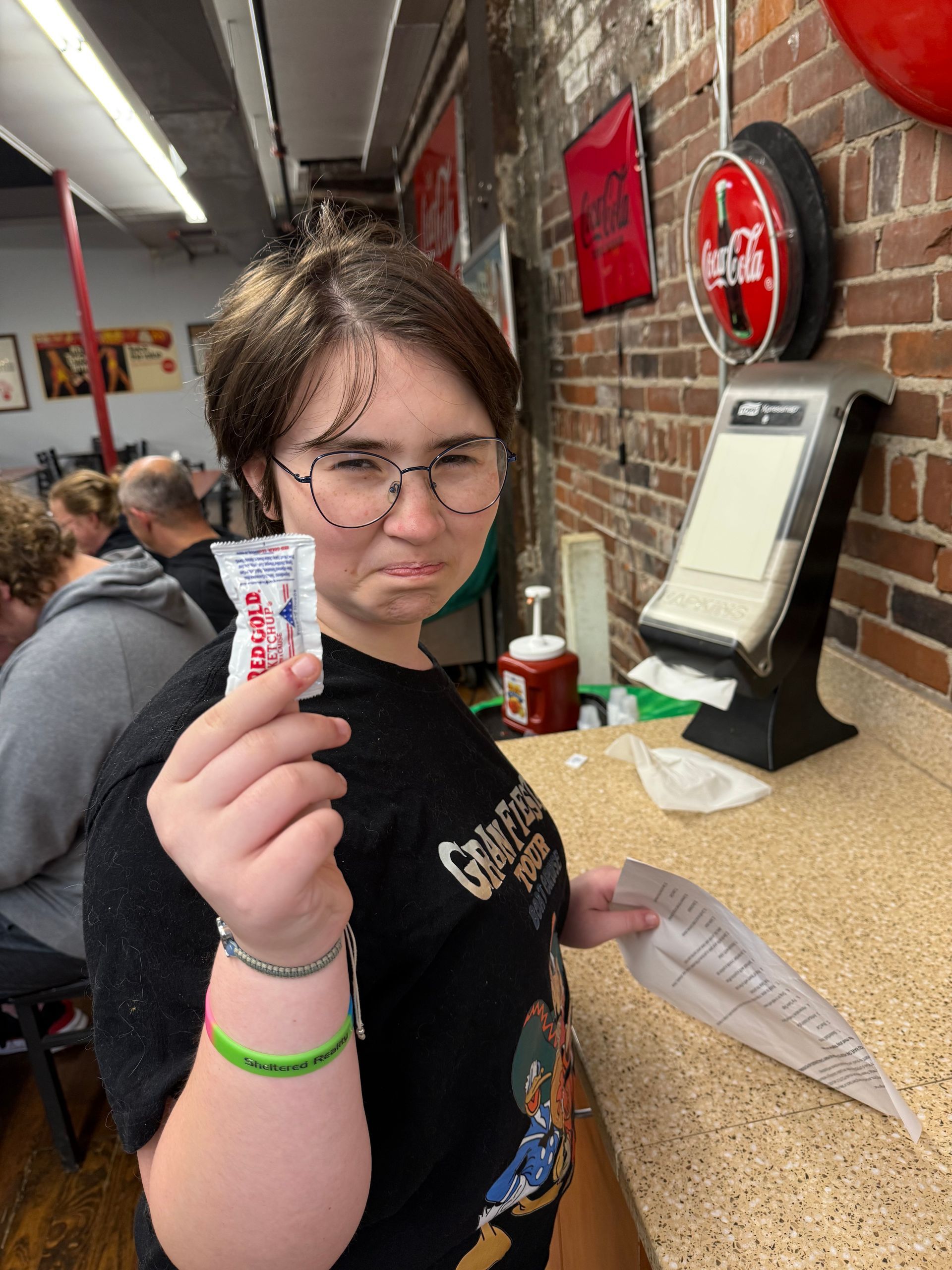 Person holding a candy bar inside a store, standing by a counter with a neutral expression.