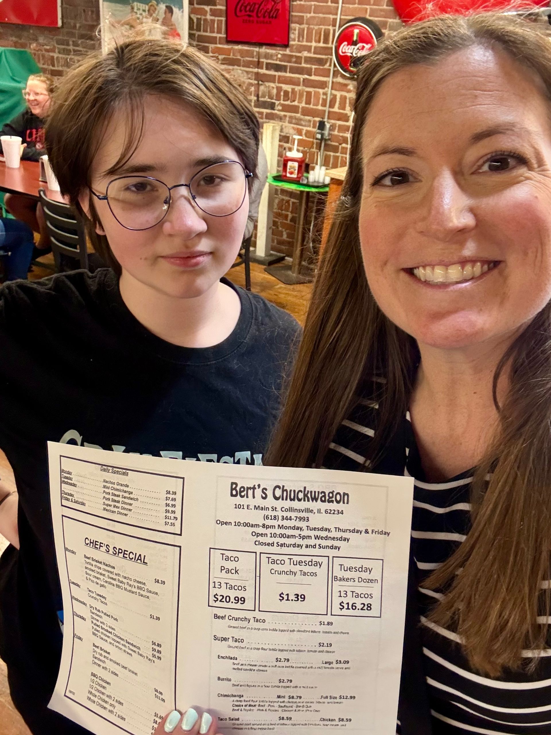 Two women smiling indoors, one holding a menu with “Let’s Cluckin” visible.