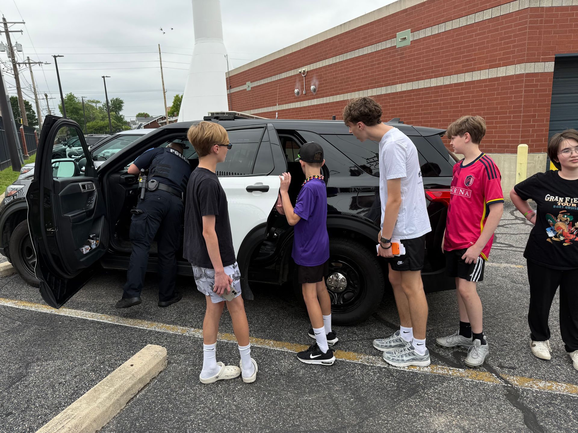 Group of people standing beside an open black SUV in a parking lot next to a brick building