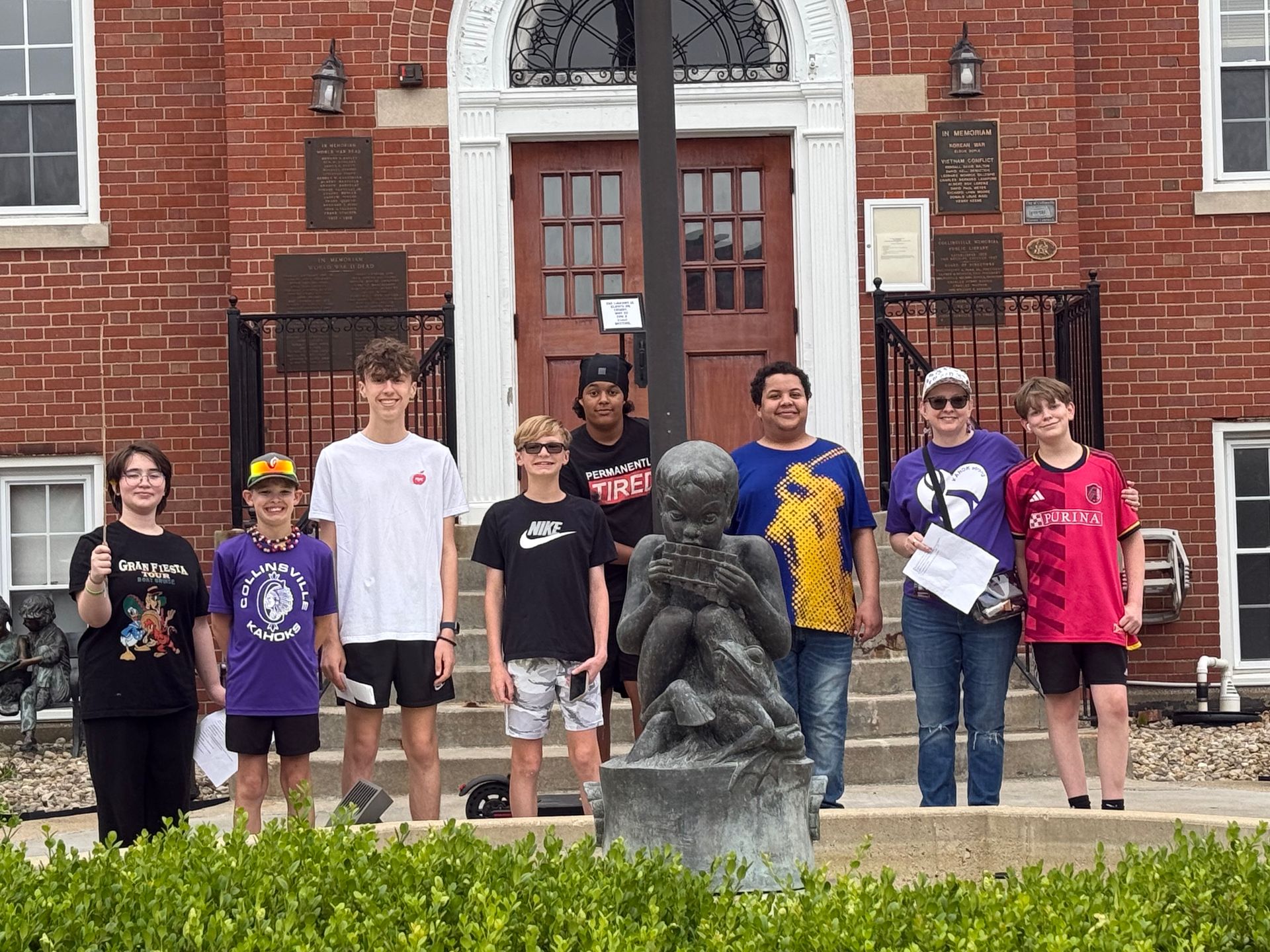 Group of students posing on steps in front of a brick building and statue outdoors