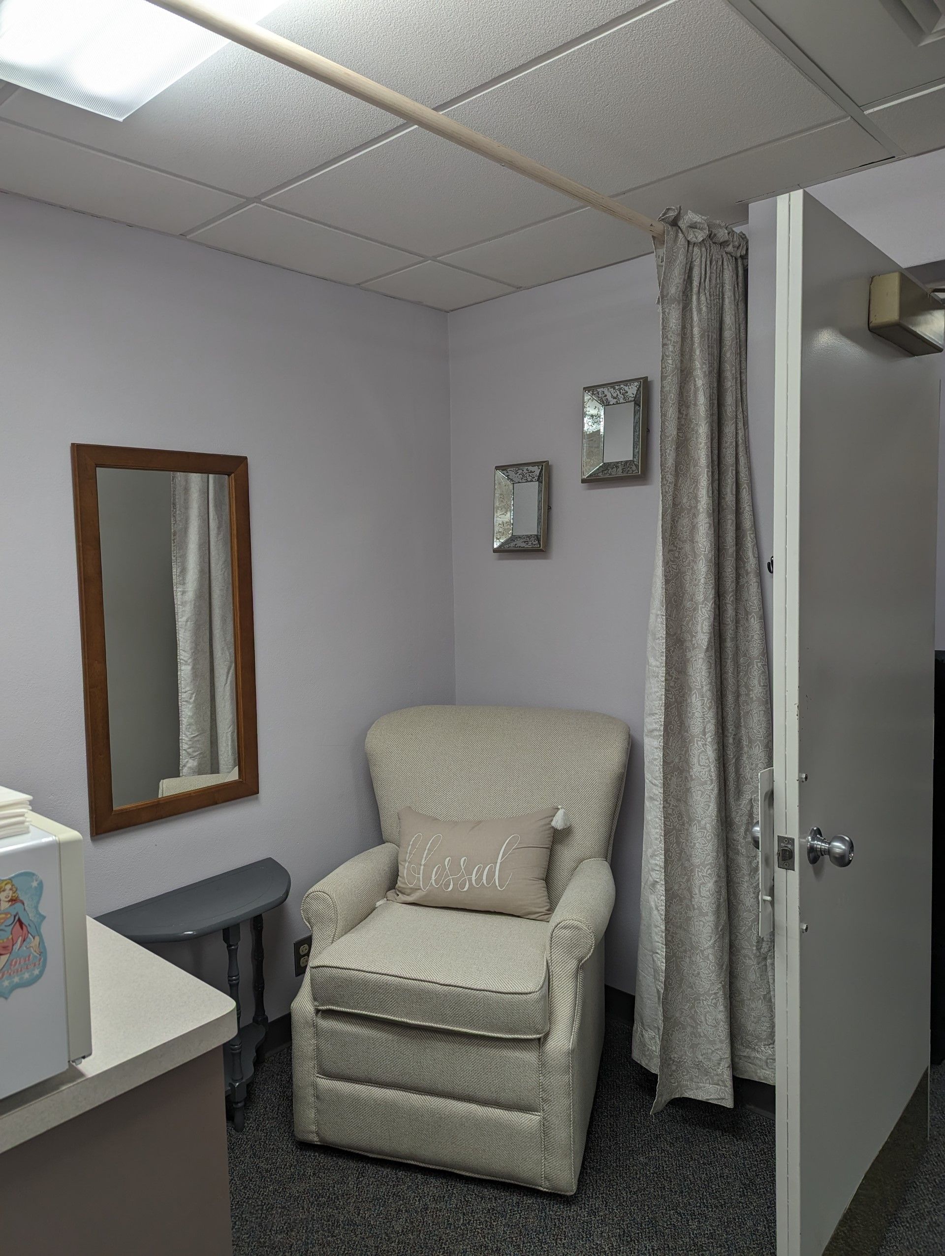 Small exam room with a beige recliner chair, wall mirror, sink counter, and privacy curtain.