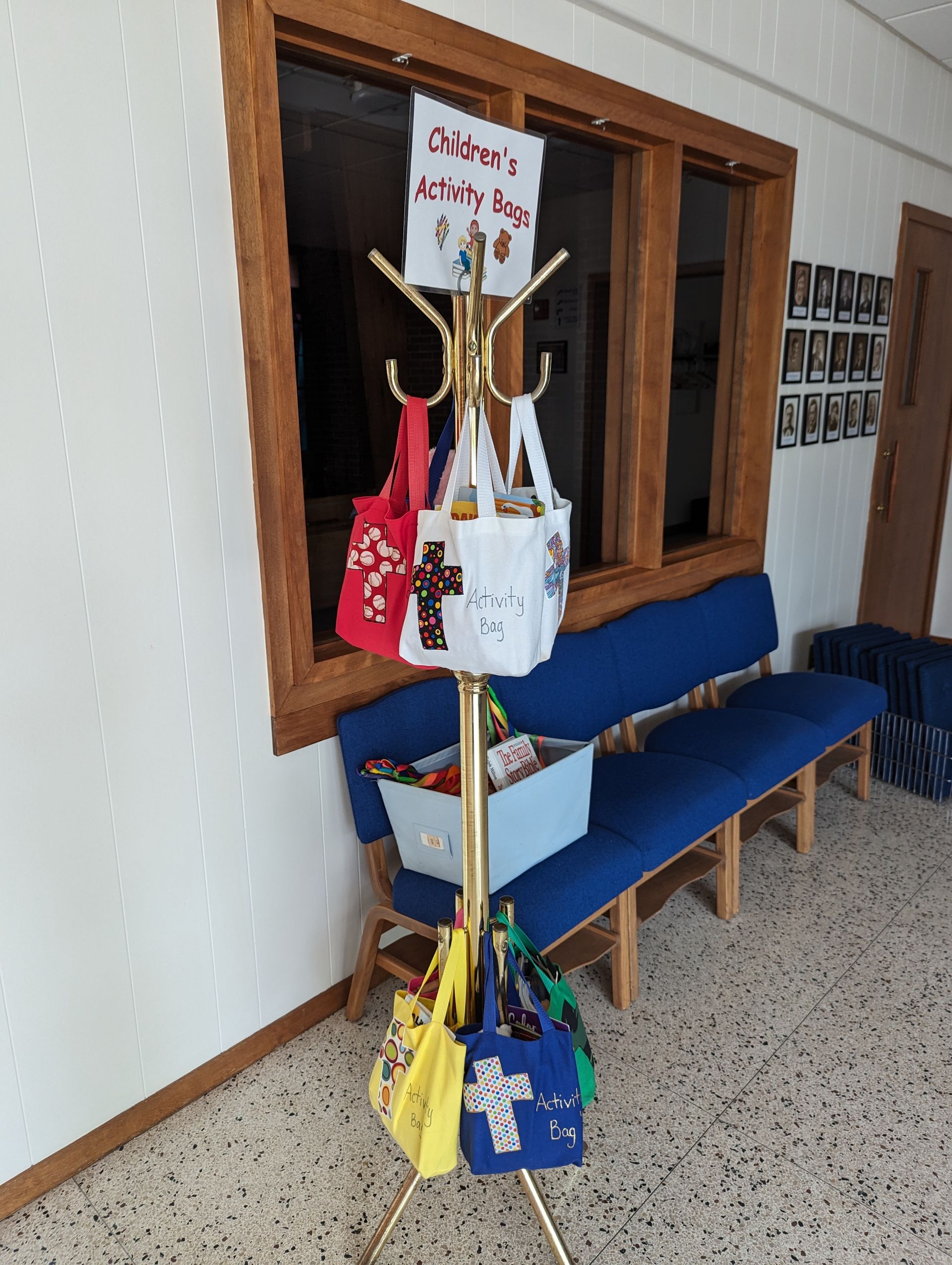 Coat rack with colorful tote bags beside a blue bench in a hallway
