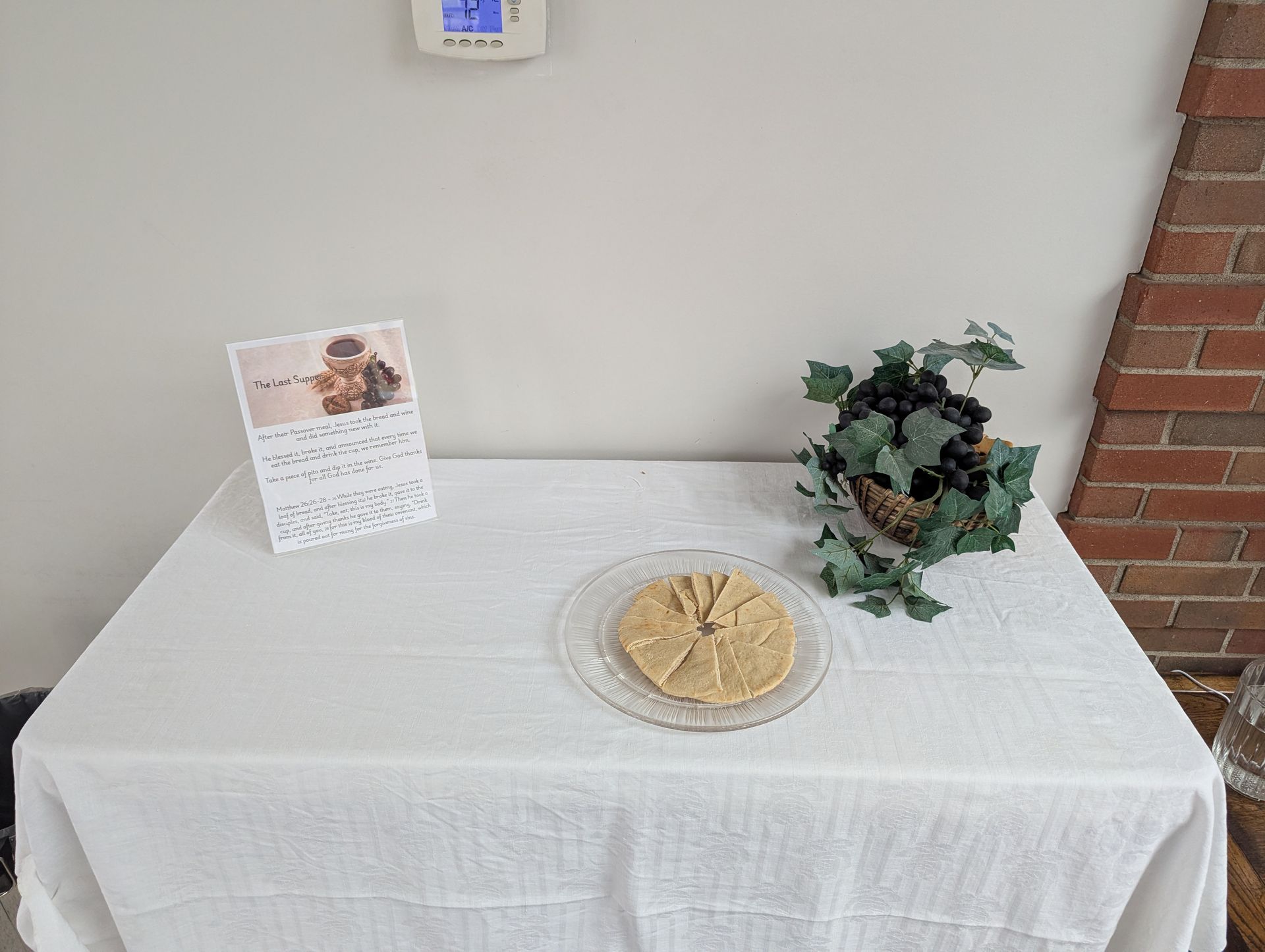 Table with a white cloth, flyer, snack platter, and potted plant against a wall