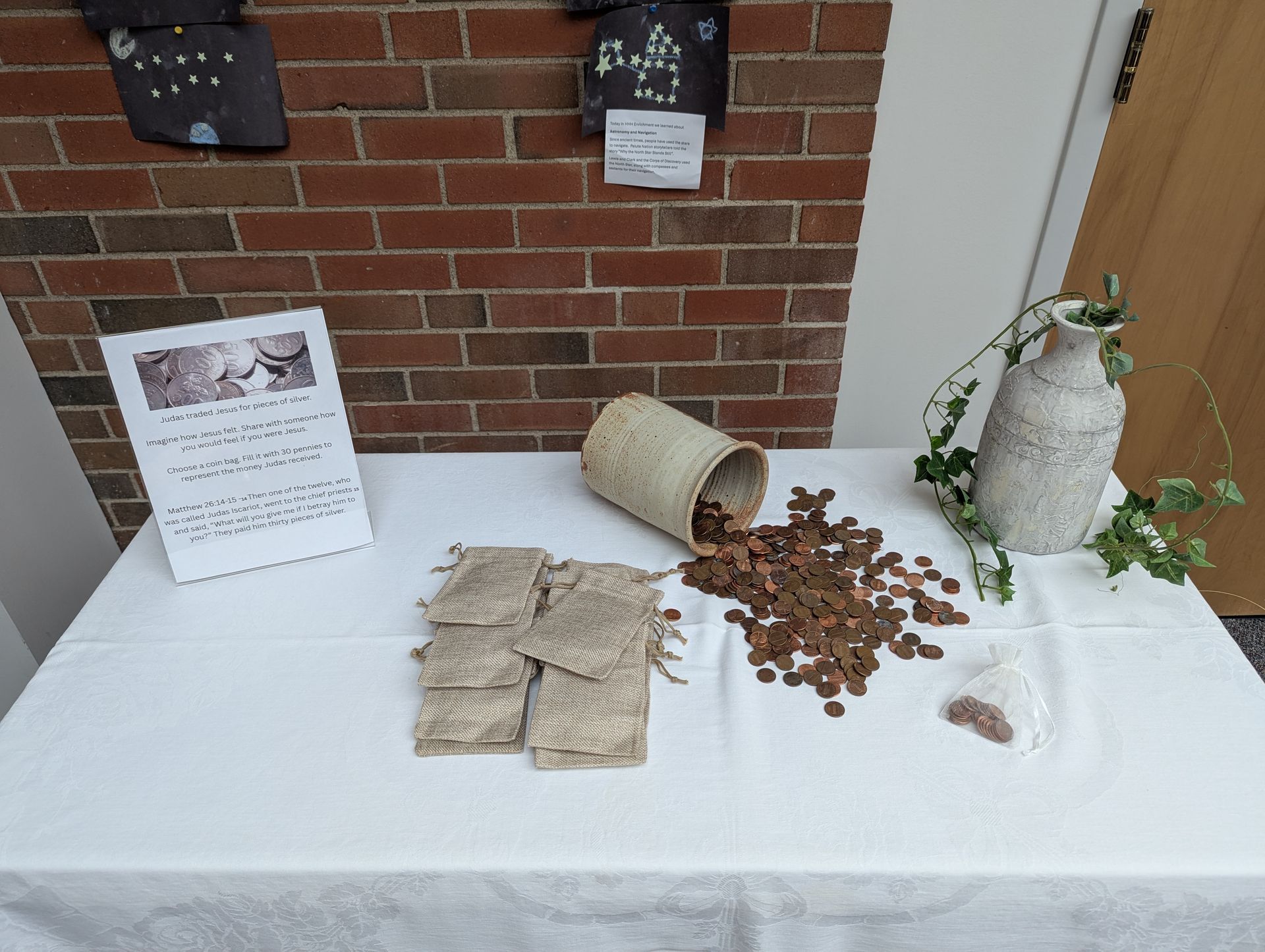 Table display with burlap sacks, spilled coffee beans, and a potted plant against a brick wall.