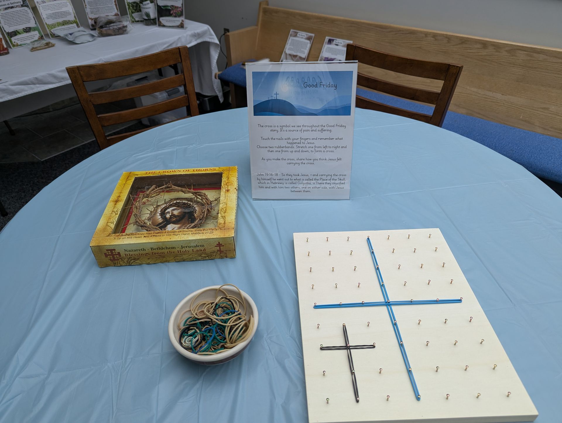 Tabletop display with candles and a sign on a blue cloth-covered table, with a wooden chair behind it