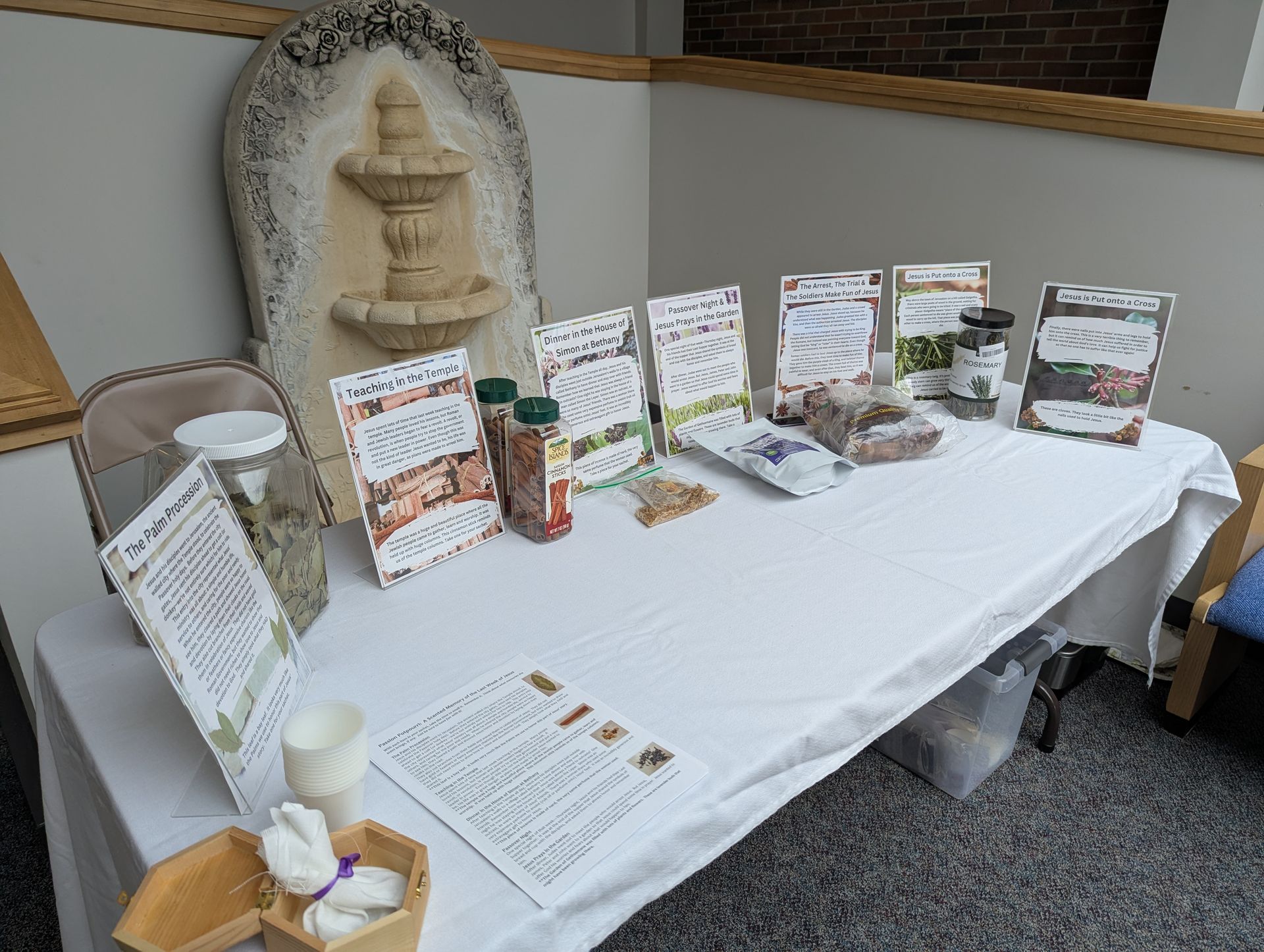 Display table with brochures, signs, and small items on a white cloth at an indoor event