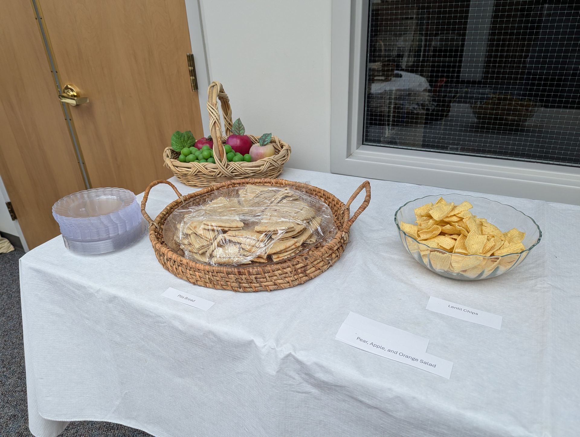 Table with wicker baskets of flatbread and chips beside a small bowl and a door; table covered in white cloth
